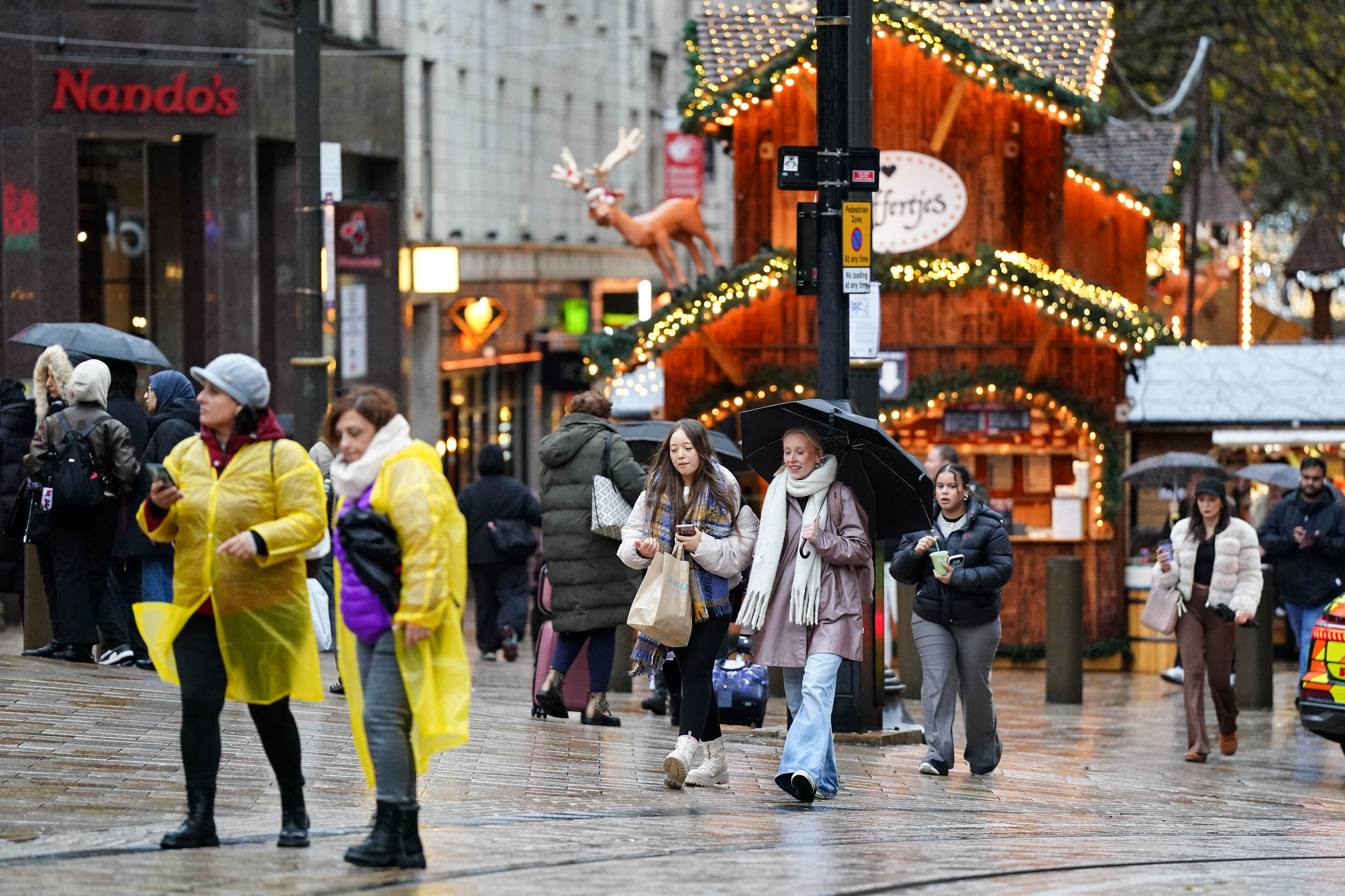 <p>People walk by Christmas markets during strong wind in Birmingham earlier in December</p>