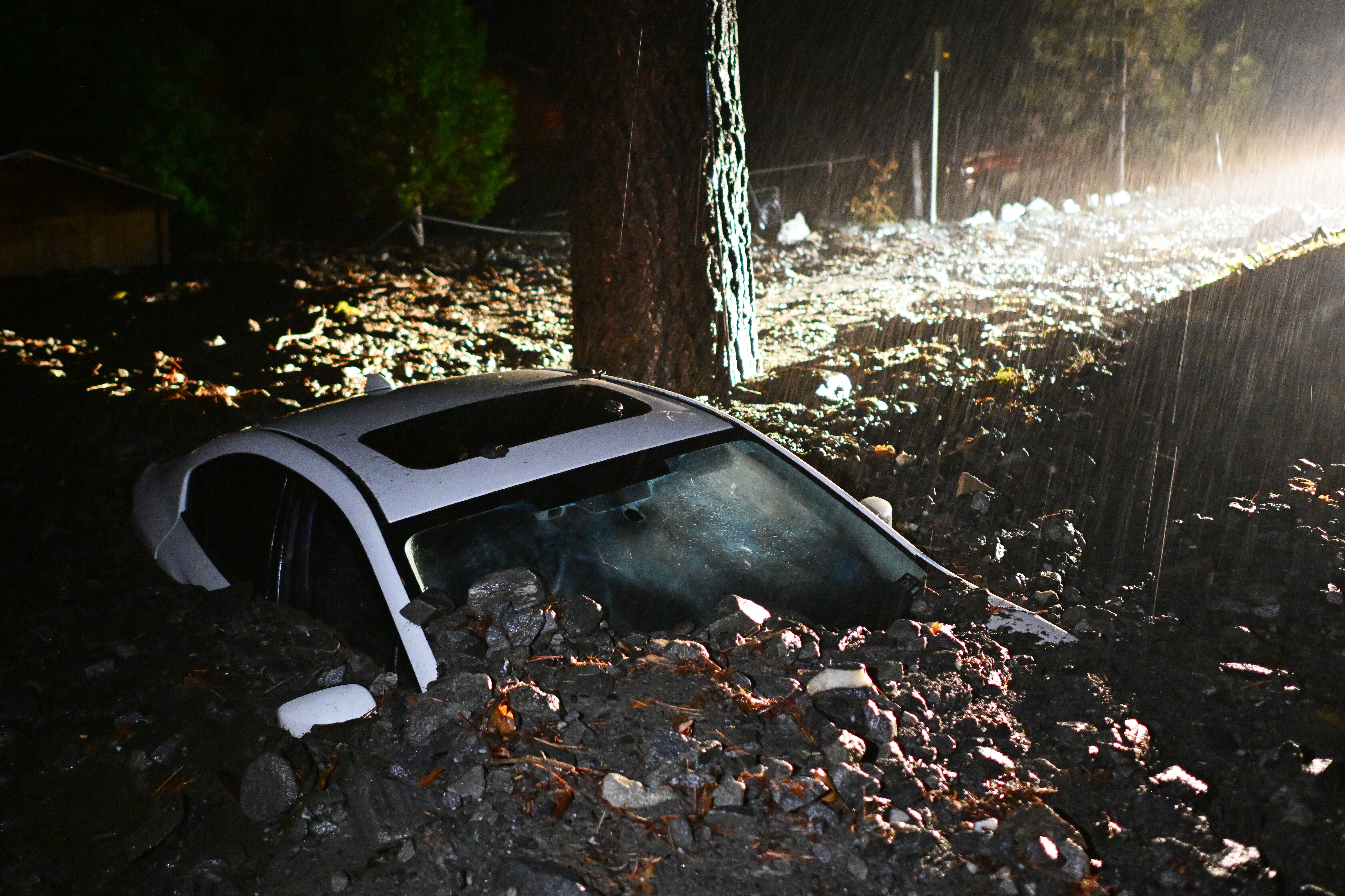 A car is buried by mud and rocks in Wrightwood, California after heavy rains from atmospheric rivers caused debris flows to sweep across the community