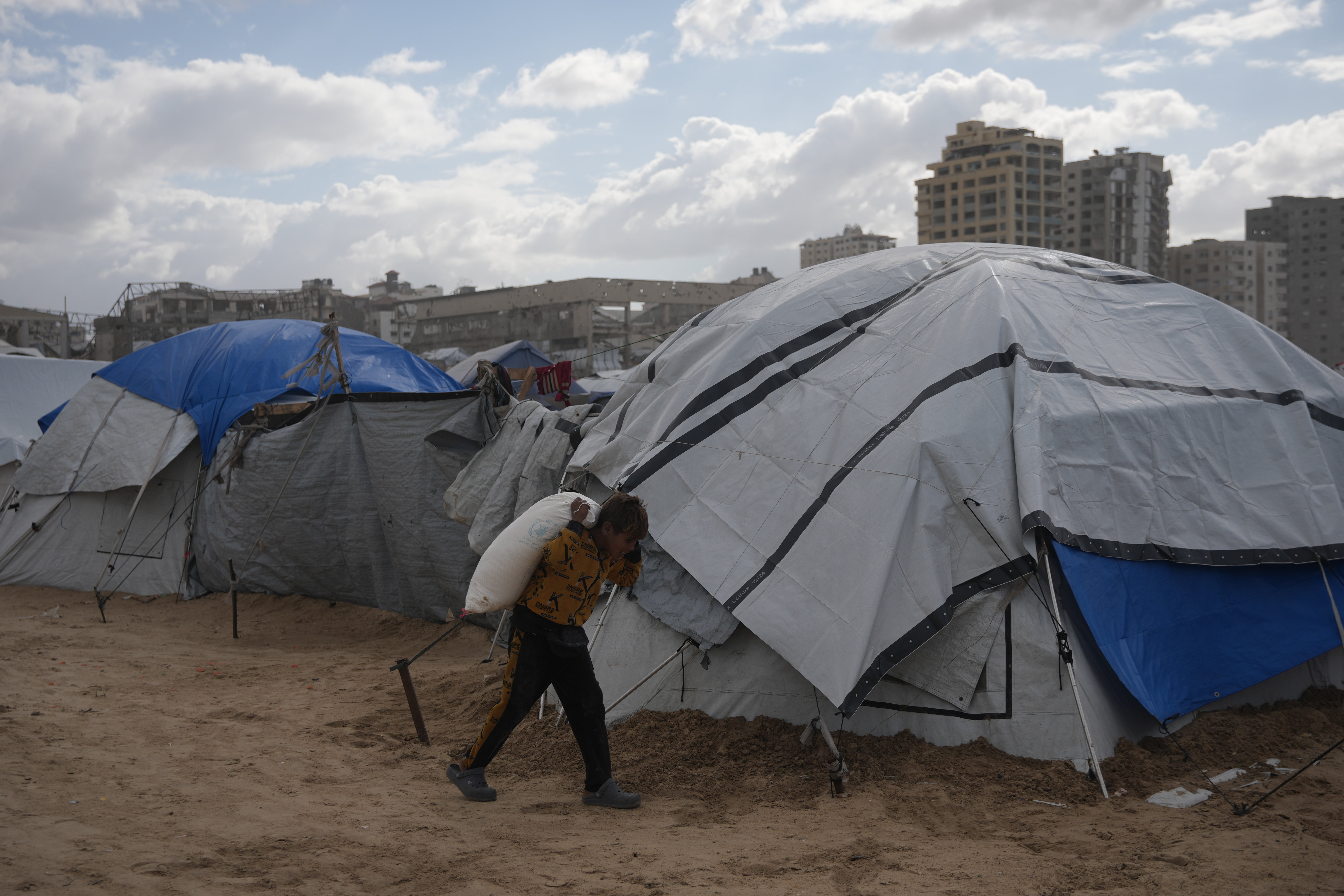 A Palestinian child carries a bag of flour on his back at a makeshift camp on the beach, in Gaza City, Sunday, Dec. 28, 2025. (AP Photo/Jehad Alshrafi)