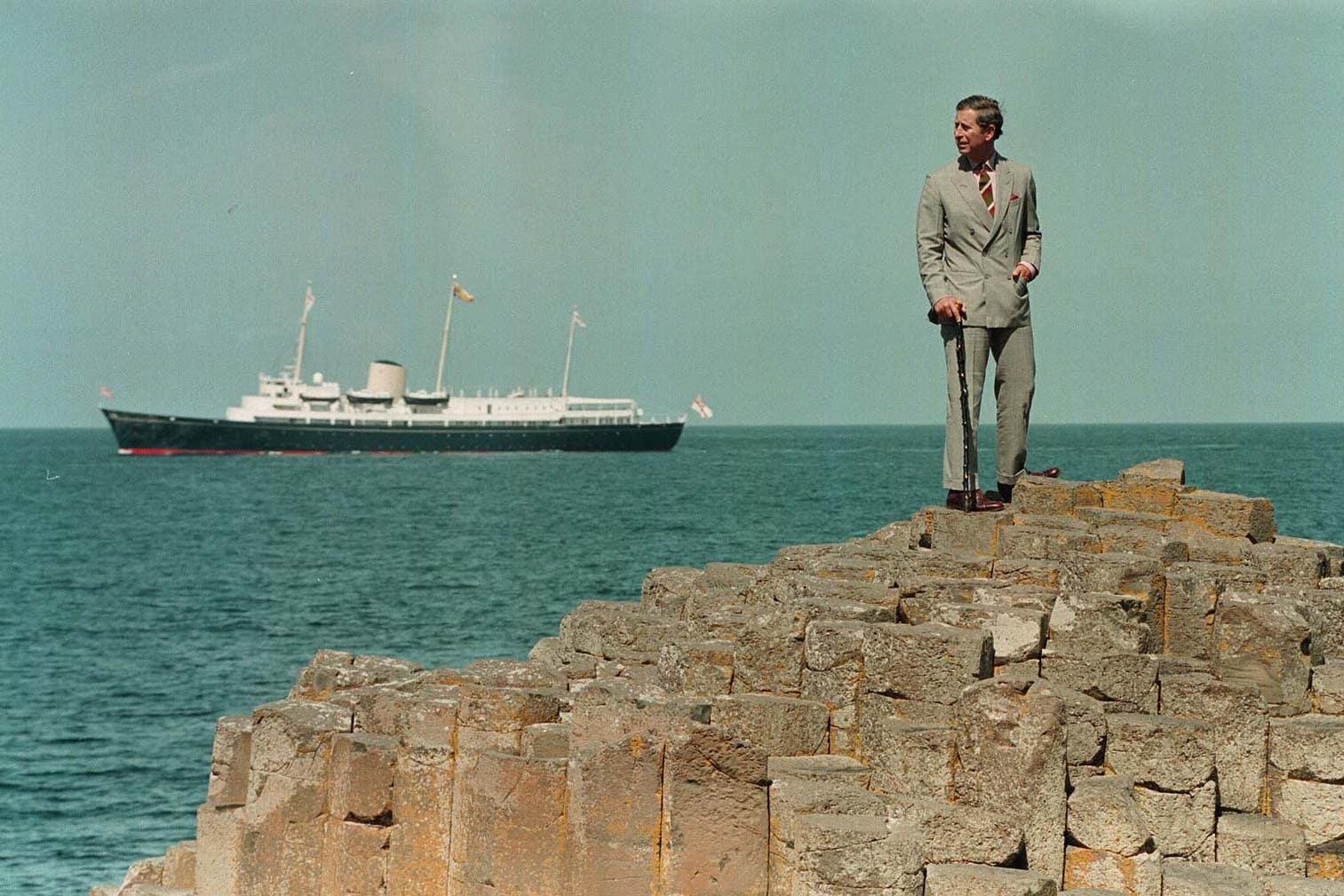 With HMS Britannia sailing behind, Charles stands on the stones of the Giant’s Causeway, Co Antrim (John Stillwell/PA)