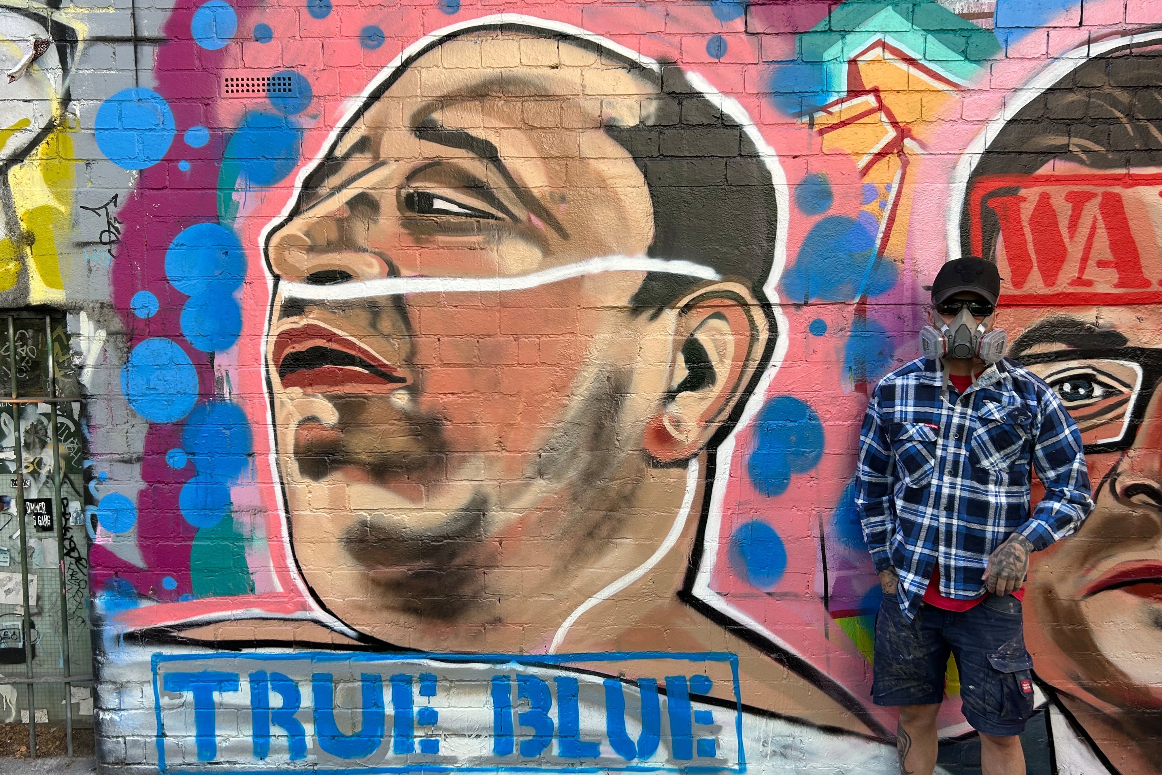 Street artist Jarrod Grech poses for a photo next to his painting of Ahmed al Ahmed, a 43-year-old Syrian-Australian shopkeeper who disarmed one of the attackers of Sydney's Bondi Beach shooting