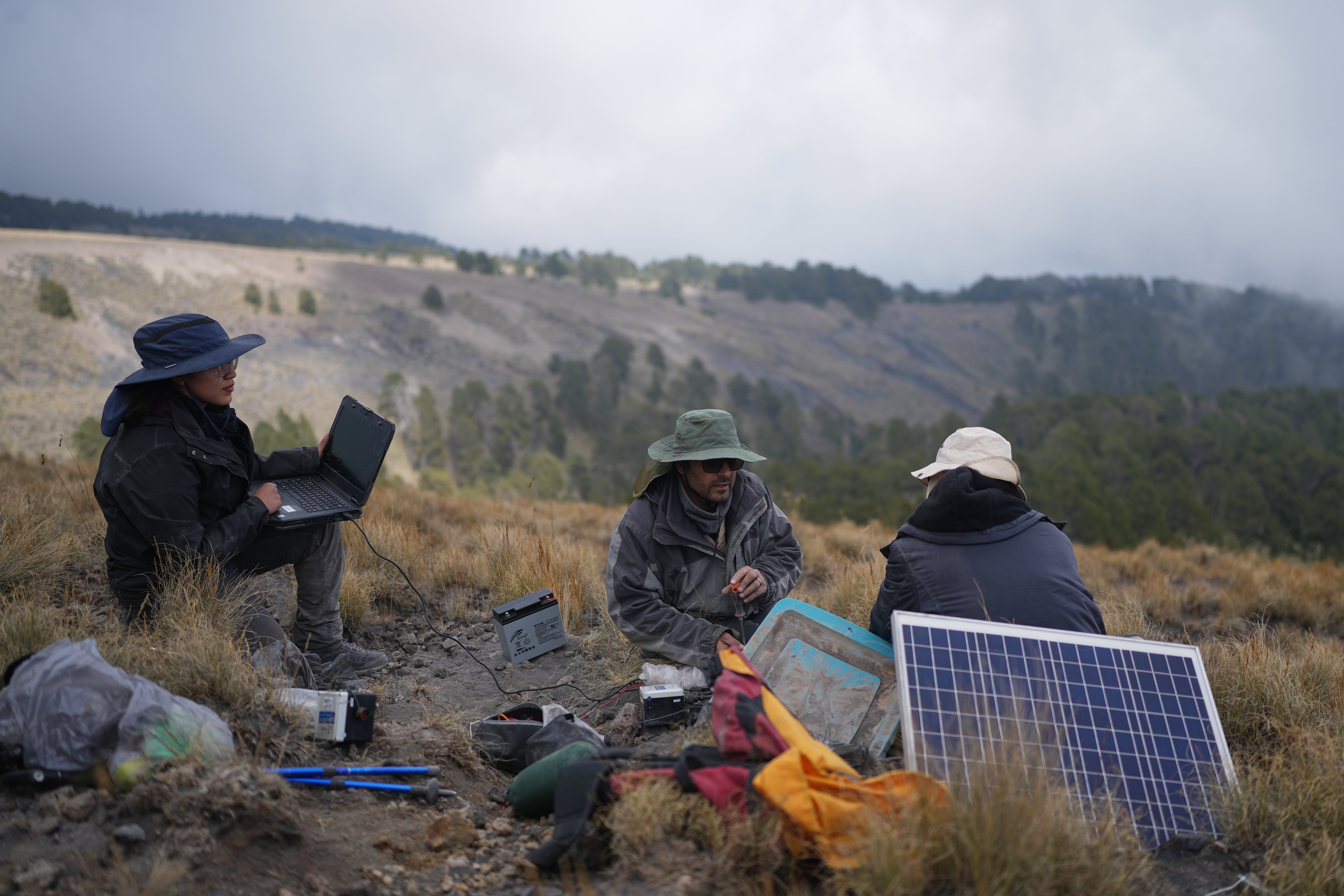 Karina Rodriguez, left, a master's student, and Marco Calo, center, a geophysicist at the National Autonomous University of Mexico (UNAM), collect information from a monitoring station on the slopes of the Popocatepetl volcano in Mexico, Friday, Dec. 5, 2025. (AP Photo/Eduardo Verdugo)