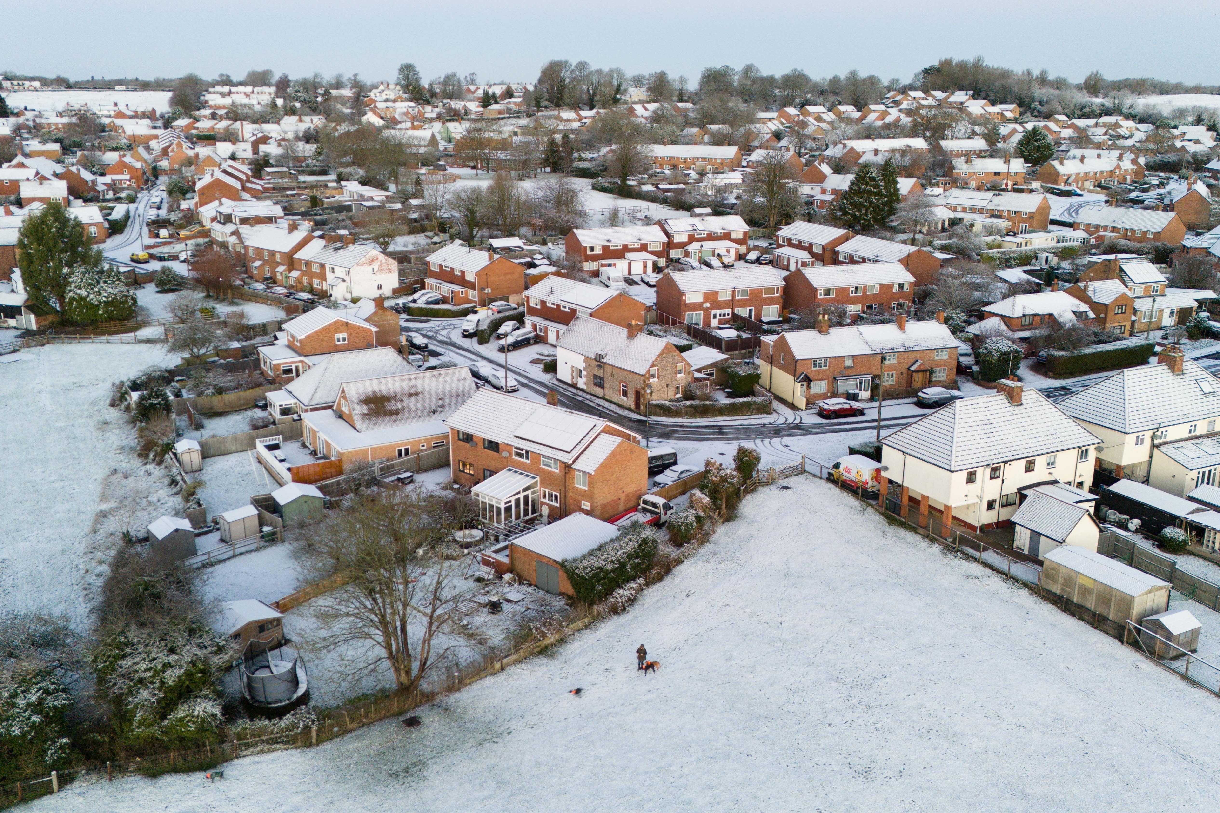 A person walks their dogs on snow-covered fields in a village in Warwickshire (Jacob KingPA)