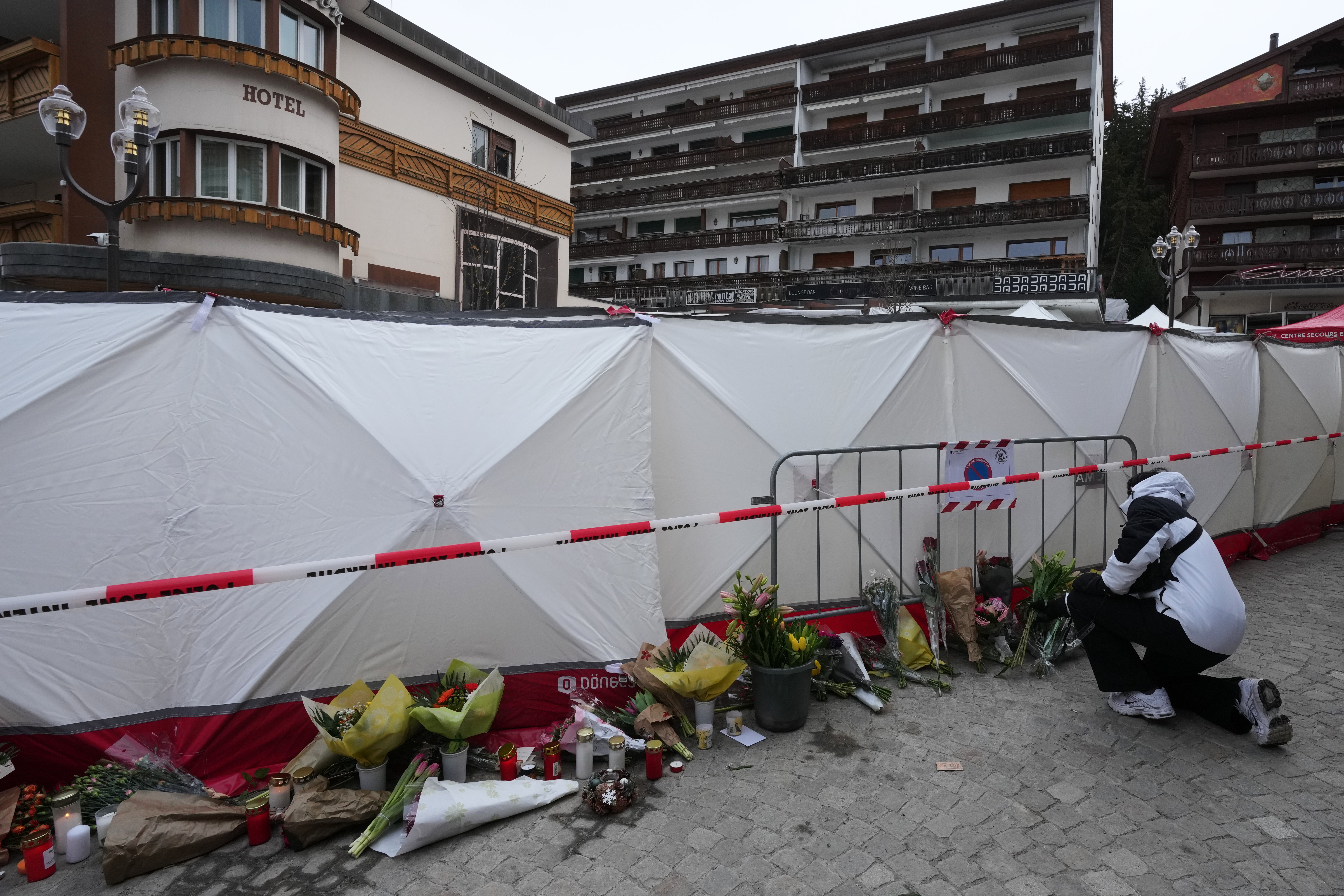 People bring flowers near the sealed off Le Constellation bar in Crans-Montana, Swiss Alps, Switzerland, Friday, Jan. 2