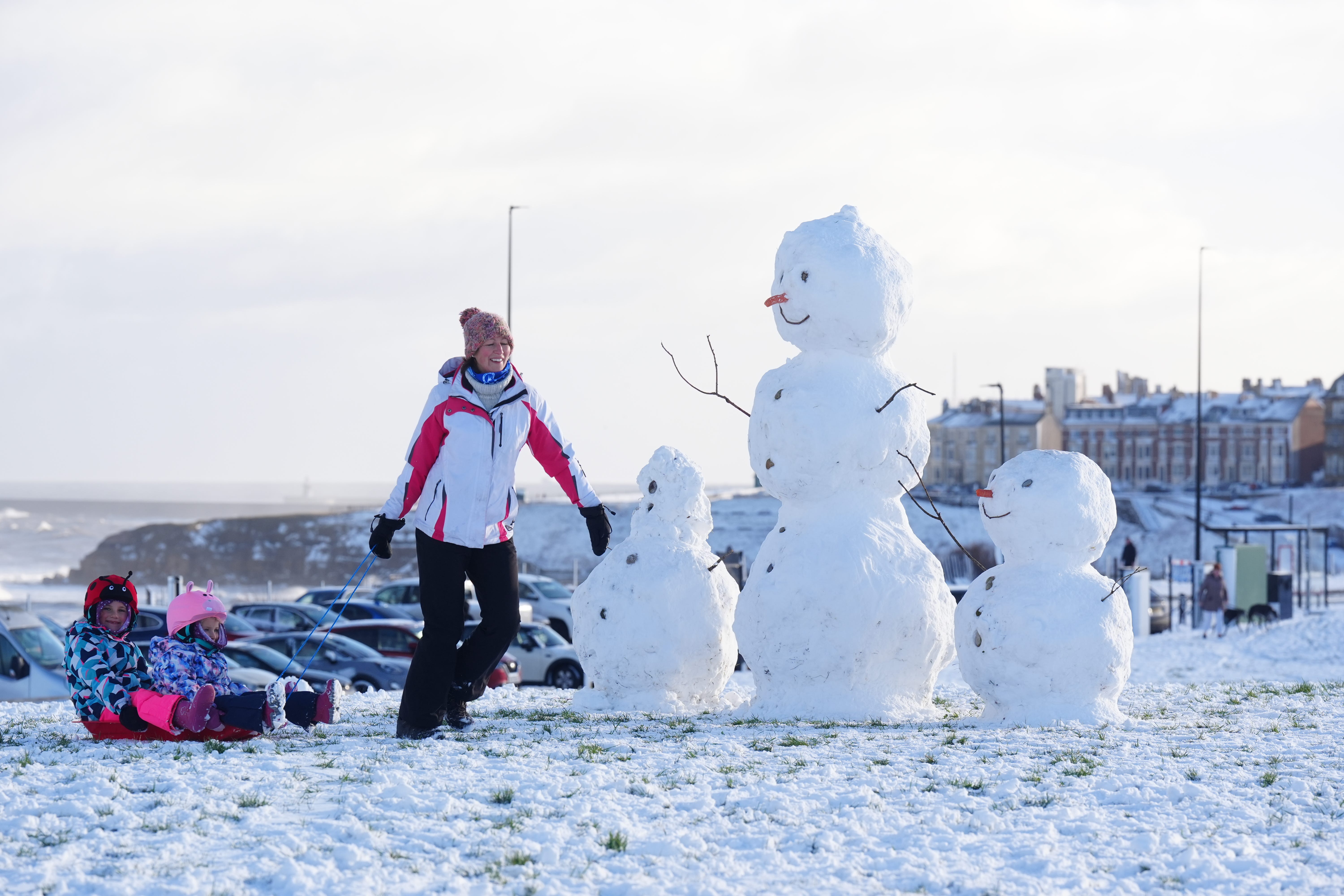 A woman pulls along two children on a sledge by snowmen at Tynemouth (Owen Humphreys/PA)