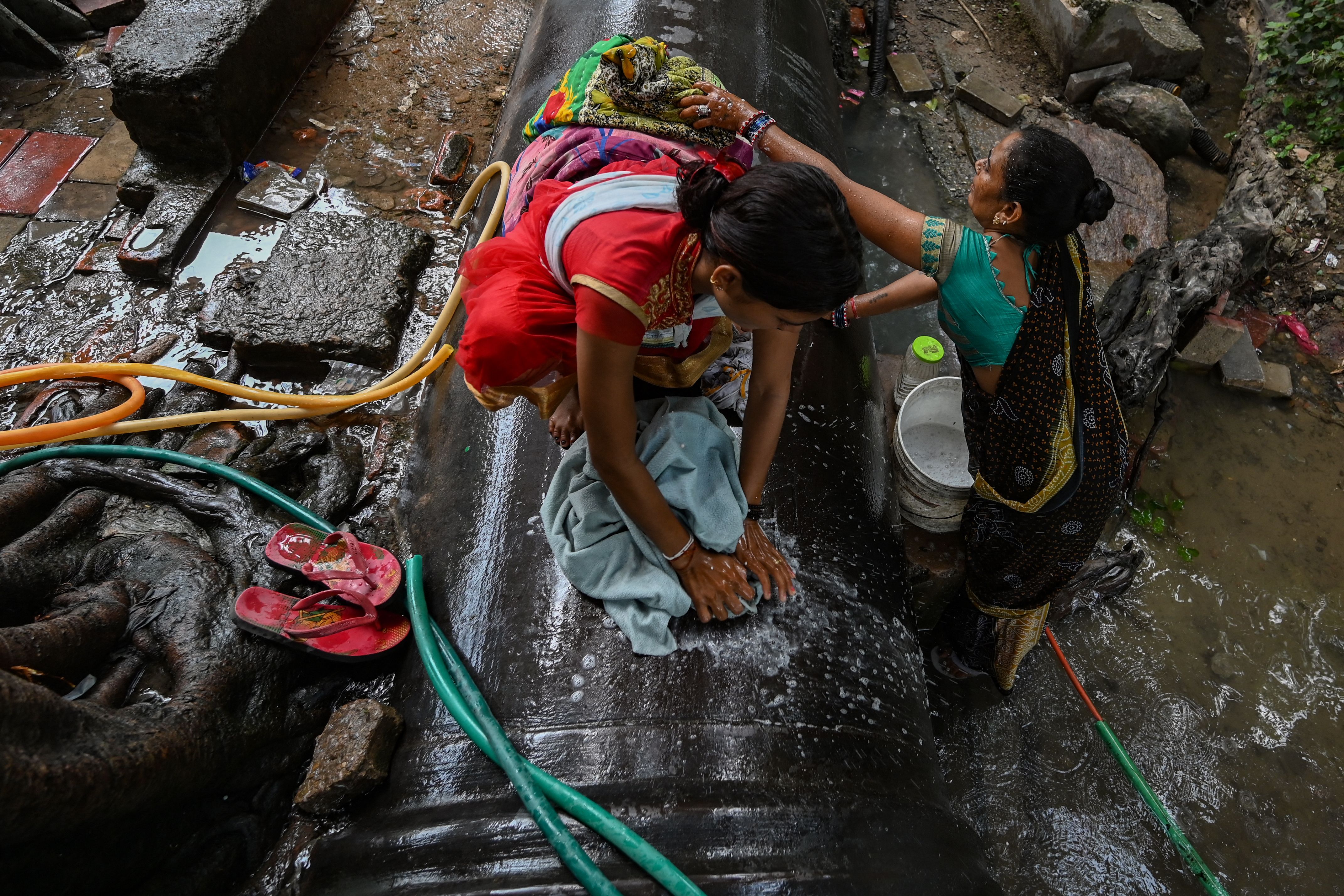 Women wash clothes with water flowing out from a leakage in a supply pipeline in Delhi on 27 September 2021