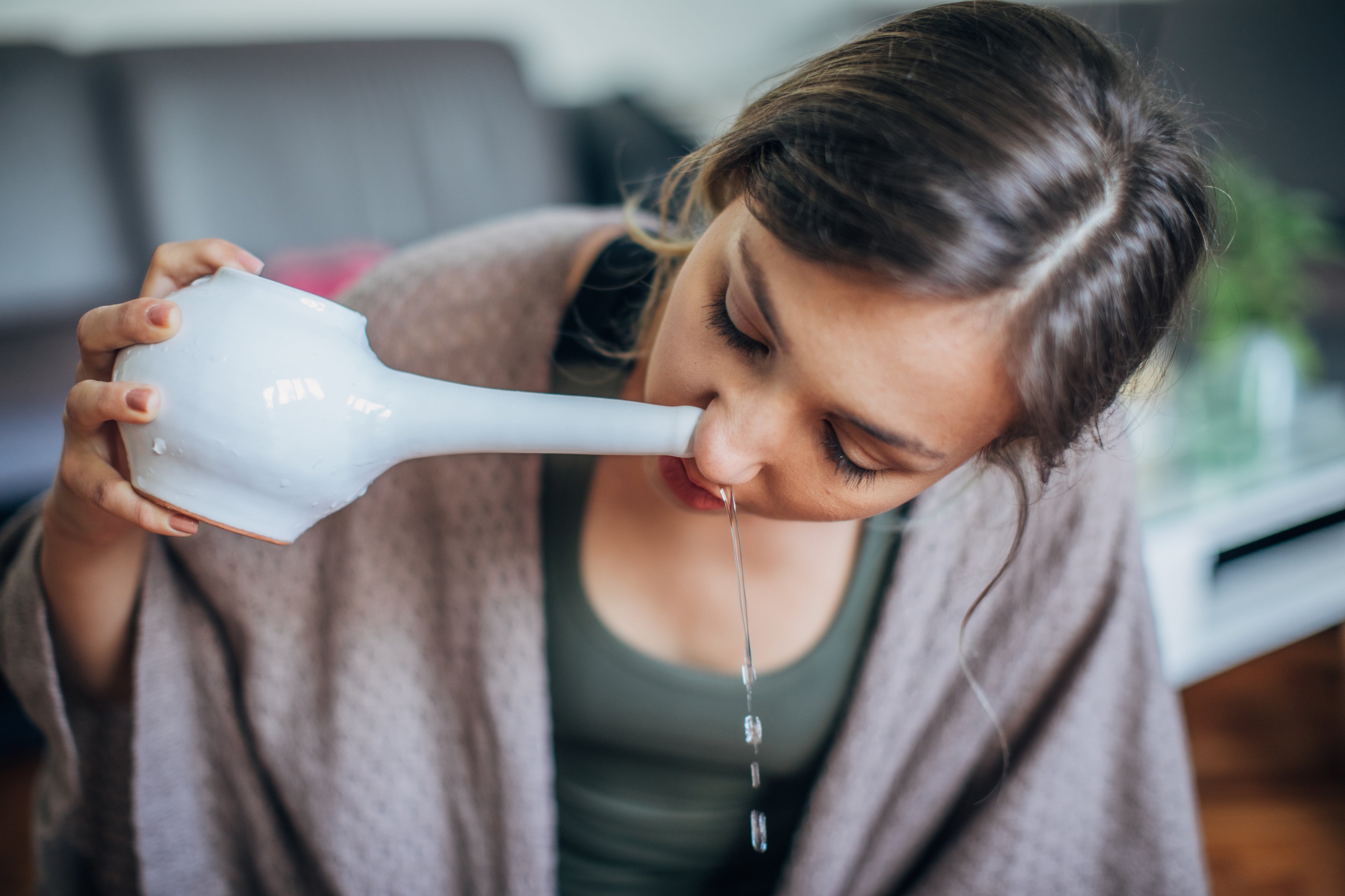<p>A young woman using neti pot at home for nasal irrigation</p>