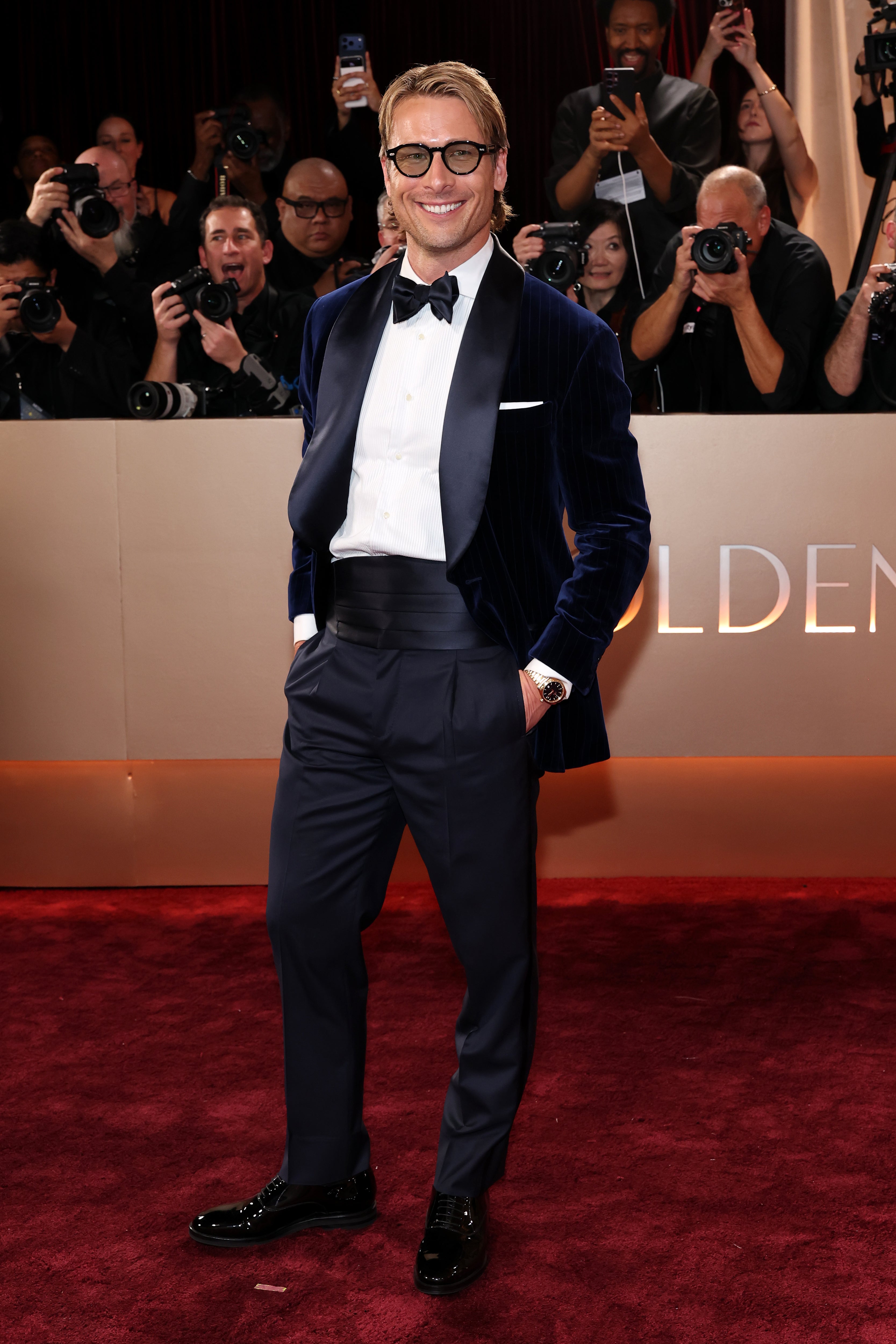 While Glen Powell attempted to spice up a classic tuxedo with a blue velvet jacket, he fell short by pairing the look with distracting tinted glasses and a slick side part in his hair