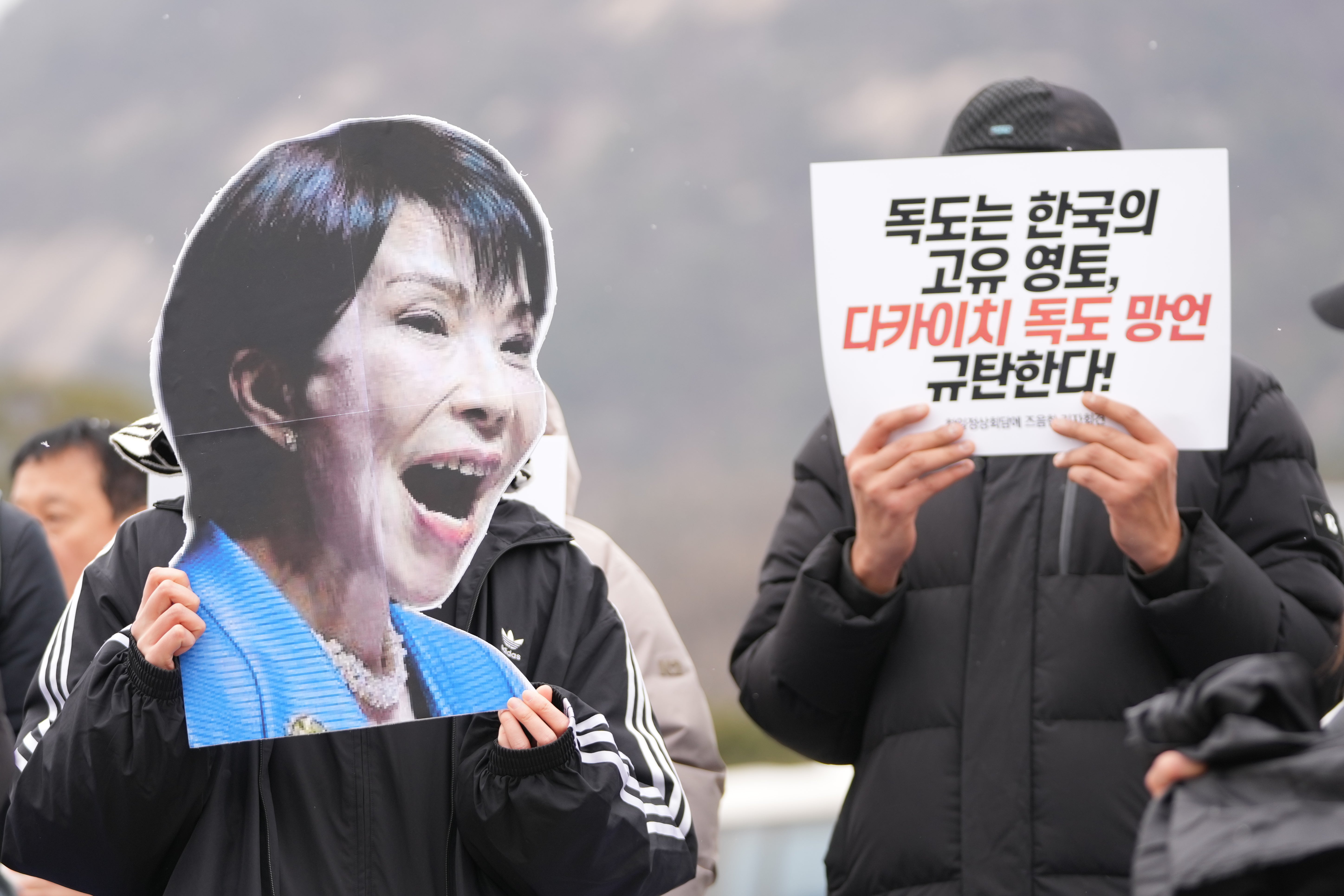 <p>A South Korean protester holds an image of Japanese prime minister Sanae Takaichi ahead of her summit meeting with South Korean president Lee Jae Myung on 12 January 2026</p>