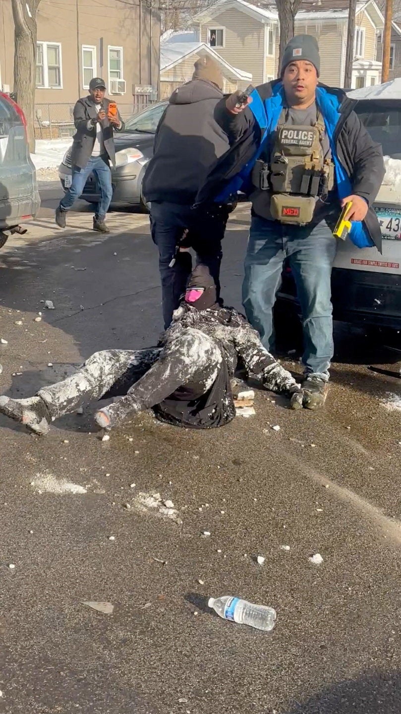 An ICE officer drags a woman through the street while another federal officer waves his firearm at a crowd of protesters in Minneapolis December 15. Immigration agents have brandished firearms at crowds and targets at least 15 times over the last year