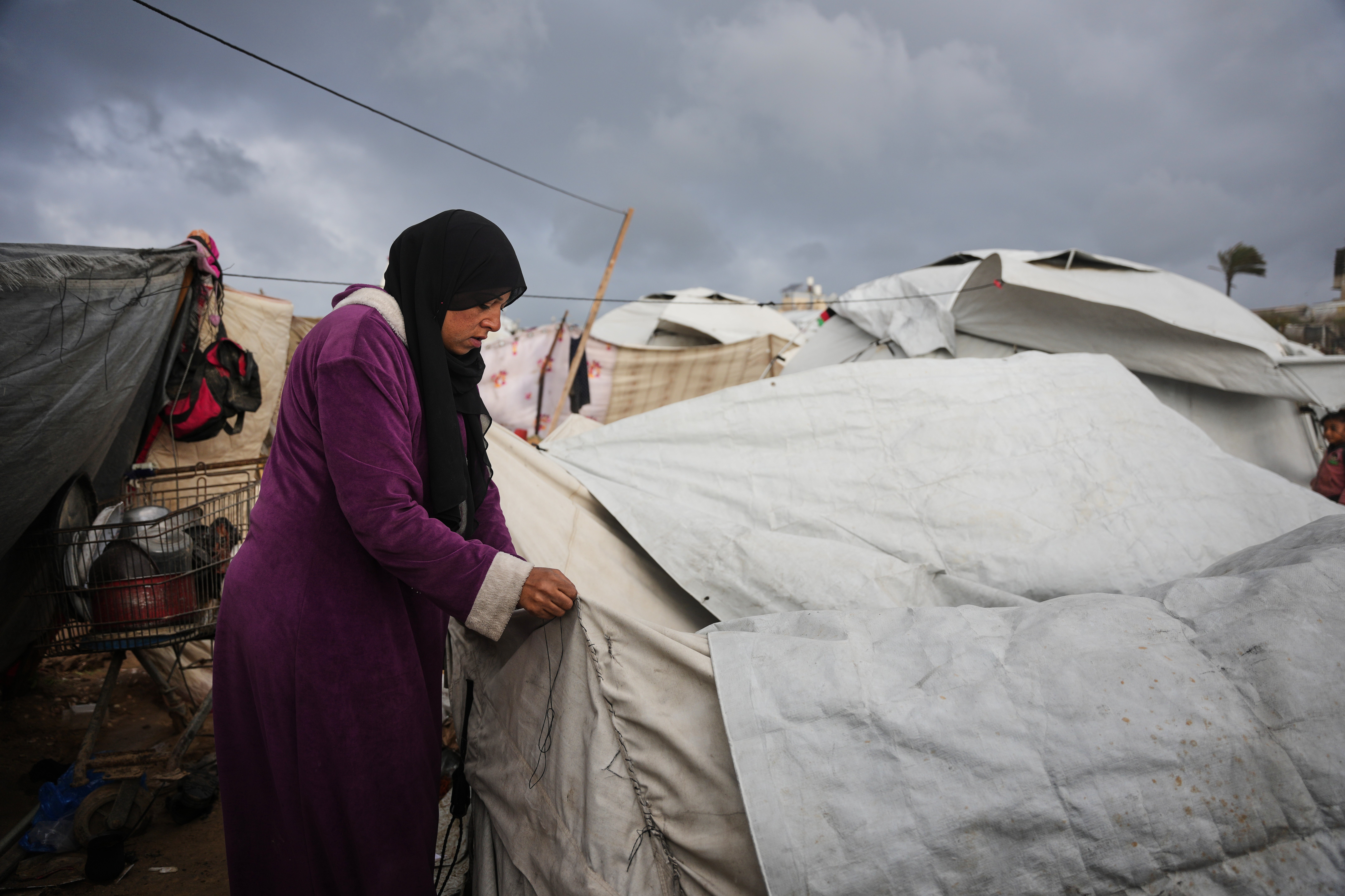 Yasmin Shalha sews her torn tent after it was damaged by a storm at a displacement camp in Zawaida