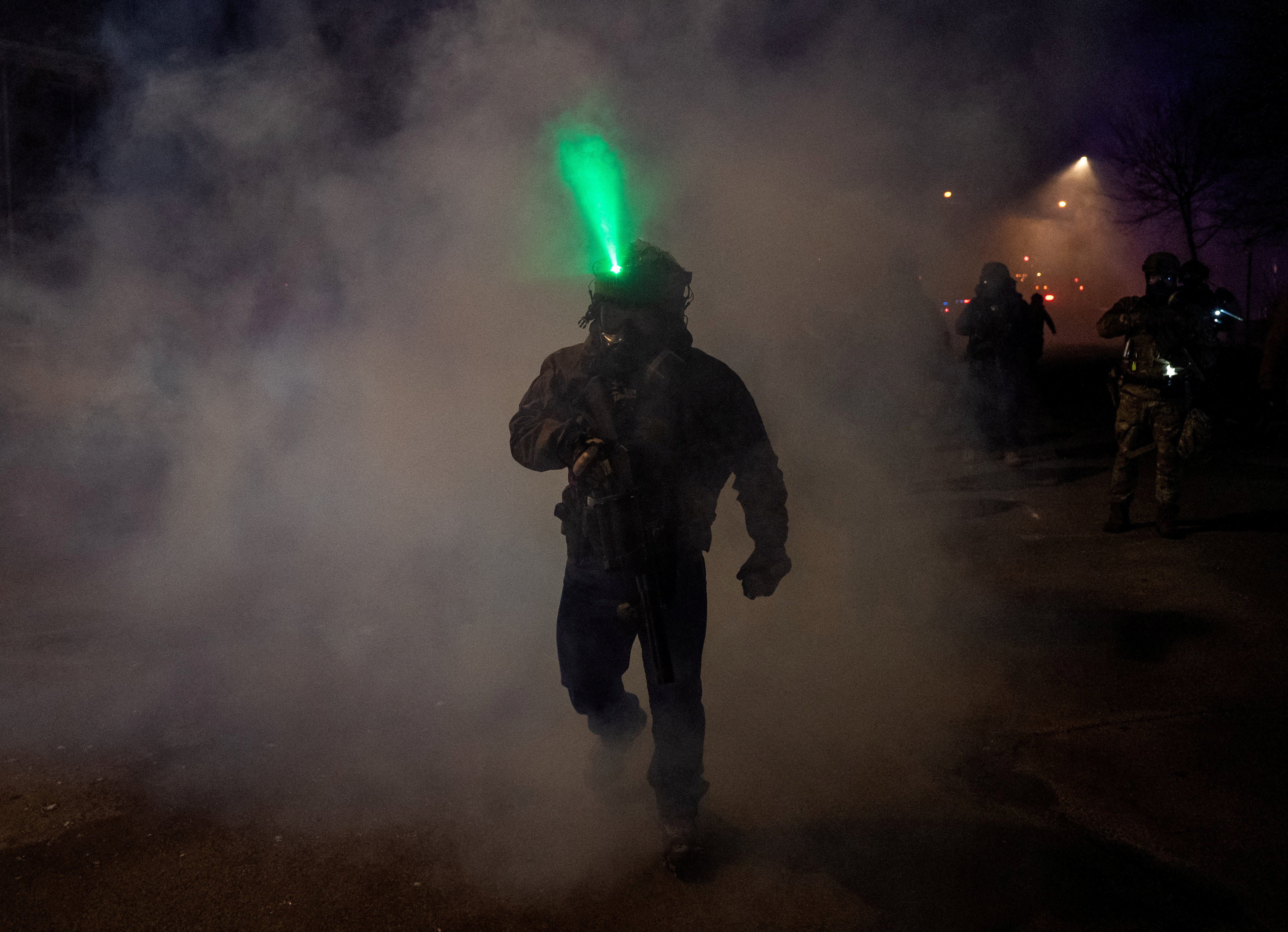 A member of federal law enforcement walks through tear gas after using the chemical on angered community members,
