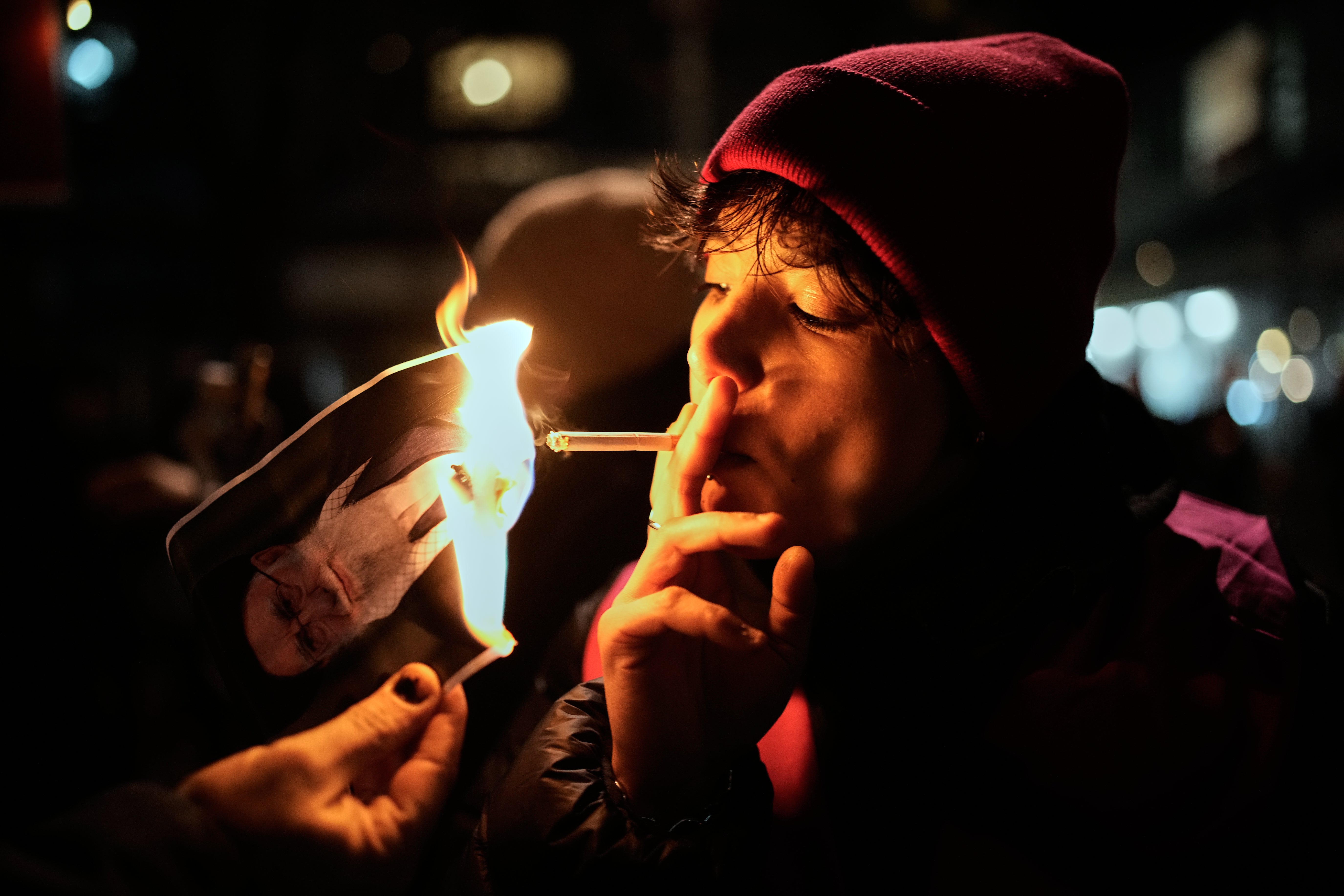 A protester lights a cigarette off a burning poster of Iran's Supreme Leader Ayatollah Ali Khamenei during a demonstration in Berlin, Germany, in support of the nationwide mass protests in Iran against the government, Wednesday, Jan. 14, 2026. (AP Photo/Ebrahim Noroozi)