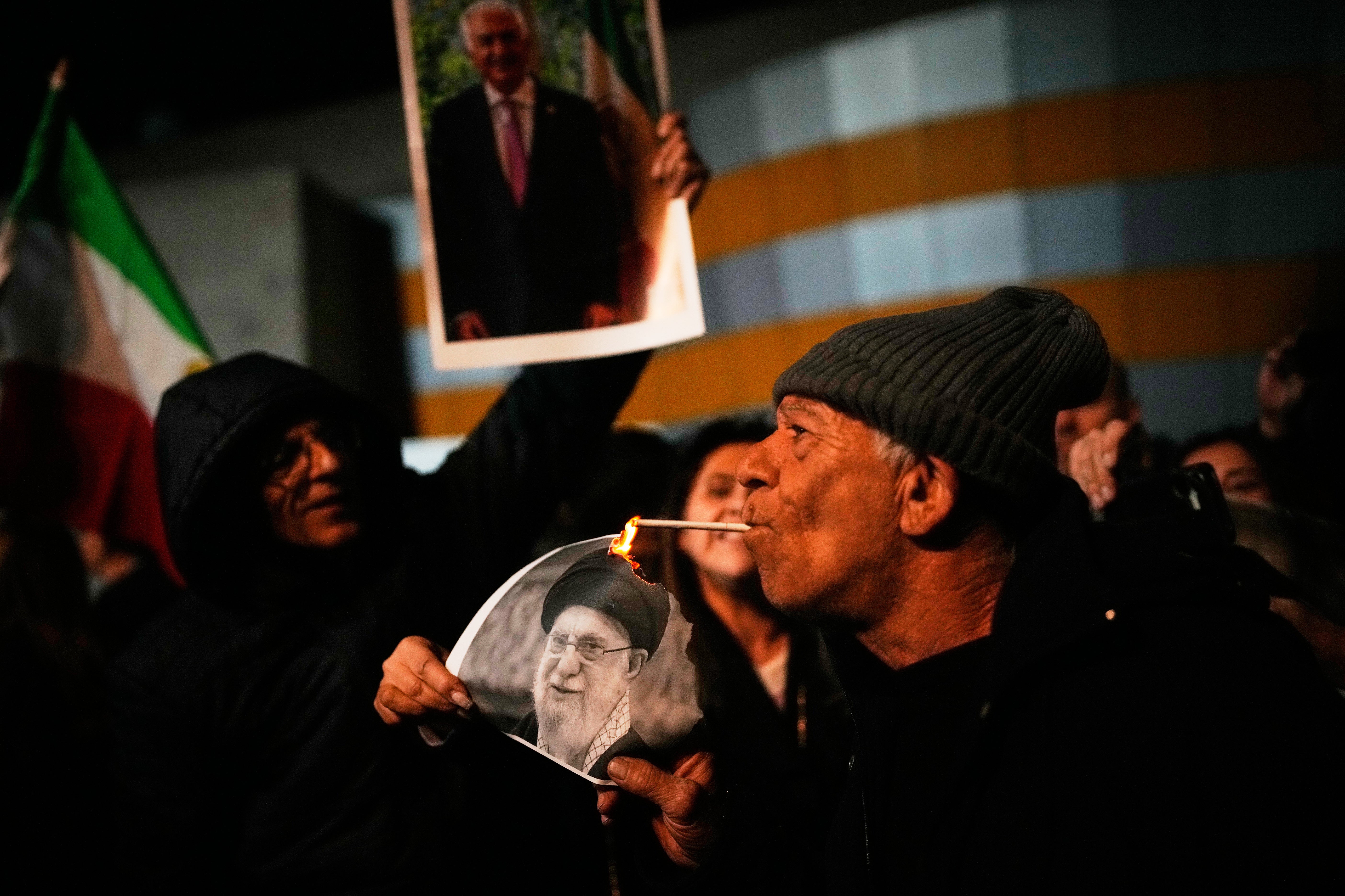 A demonstrator lights a cigarette with a burning poster depicting Supreme Leader Ayatollah Ali Khamenei during a rally in support of Iran's anti-government protests, in Holon, Israel Wednesday, Jan. 14, 2026. (AP Photo/Ohad Zwigenberg)