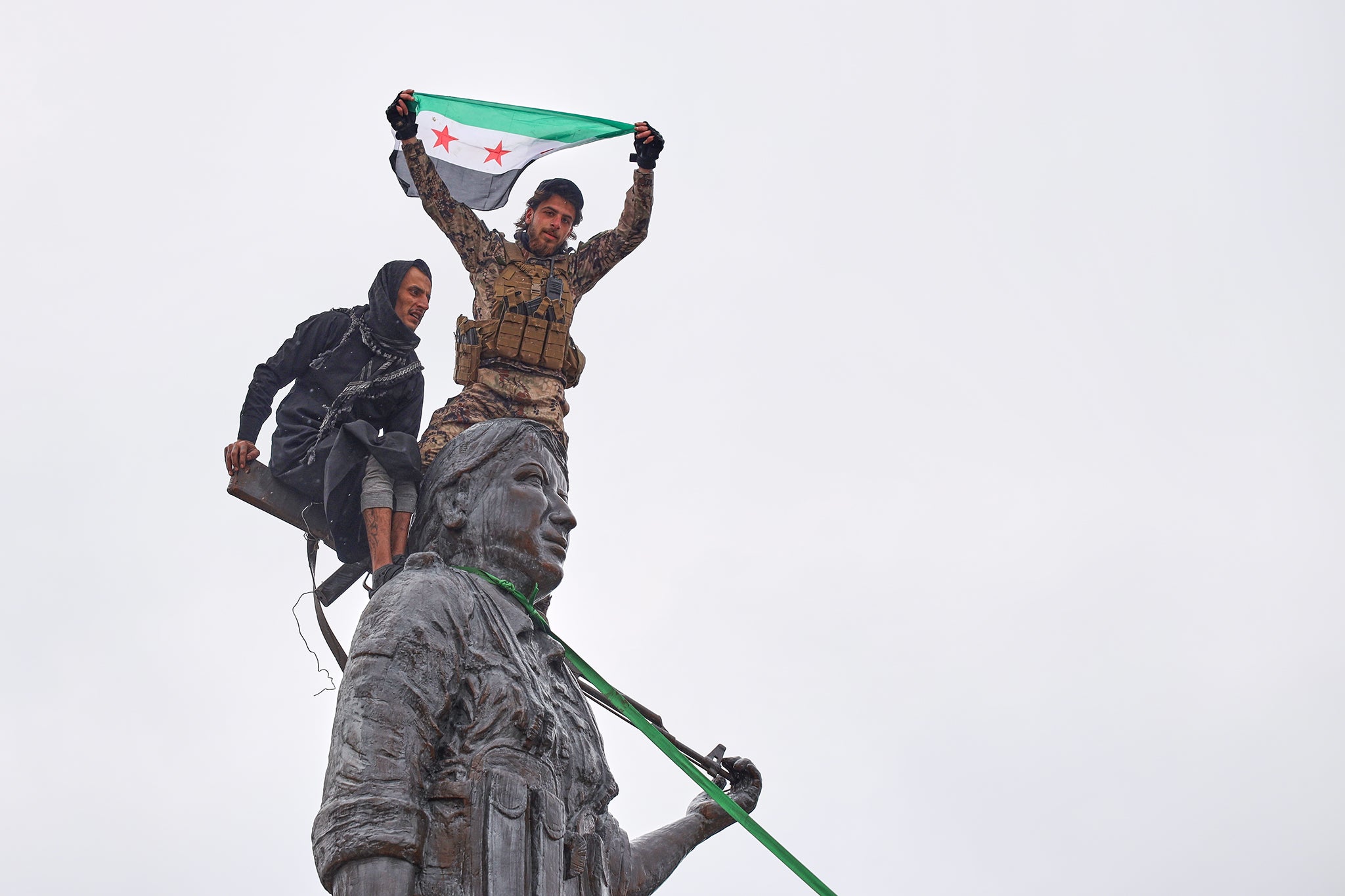 Syrian government soldiers wave a Syrian flag after climbing atop a statue of a female Kurdish fighter, following the takeover of the town from US-backed Syrian Democratic Forces (SDF