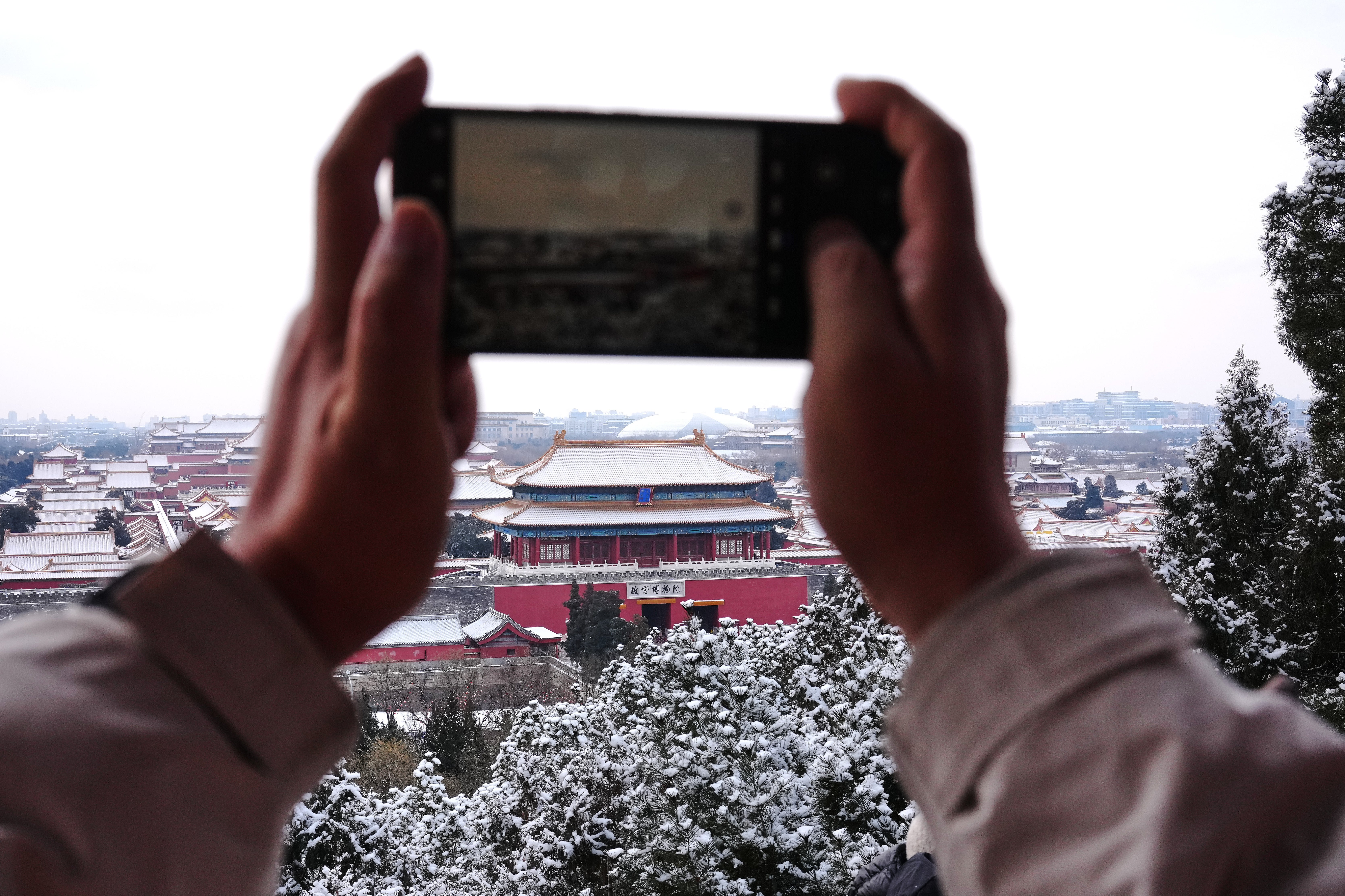 A visitor uses a smartphone to film the snow-covered Forbidden City from a pavilion at the Jingshan Park a day after the snow fall, in Beijing, Sunday, Jan. 18, 2026. (AP Photo/Andy Wong)
