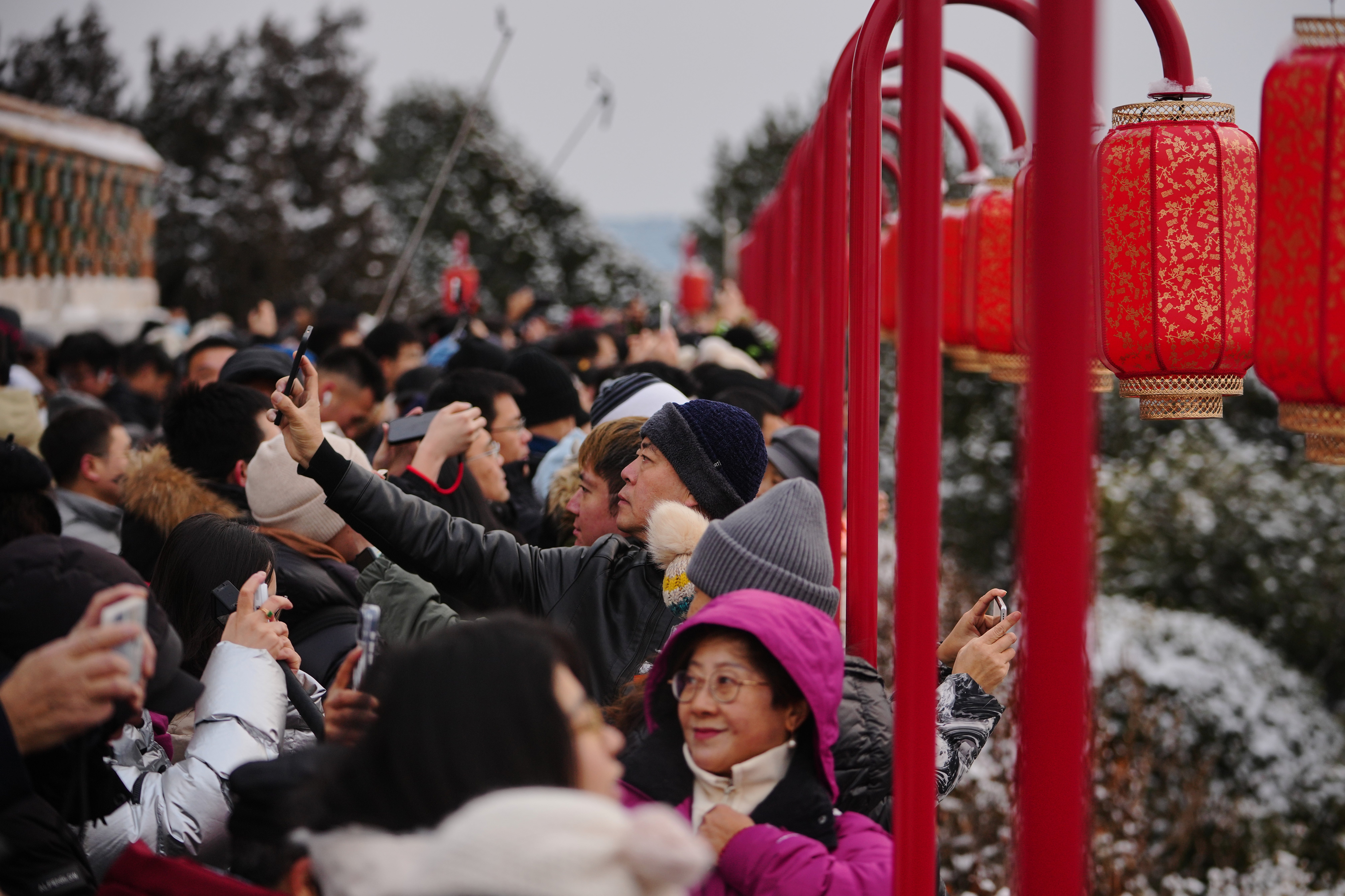 People catch a sight of the snow-covered Forbidden City from a pavilion with lantern decorations at the Jingshan Park a day after the snow fall, in Beijing, Sunday, Jan. 18, 2026. (AP Photo/Andy Wong)