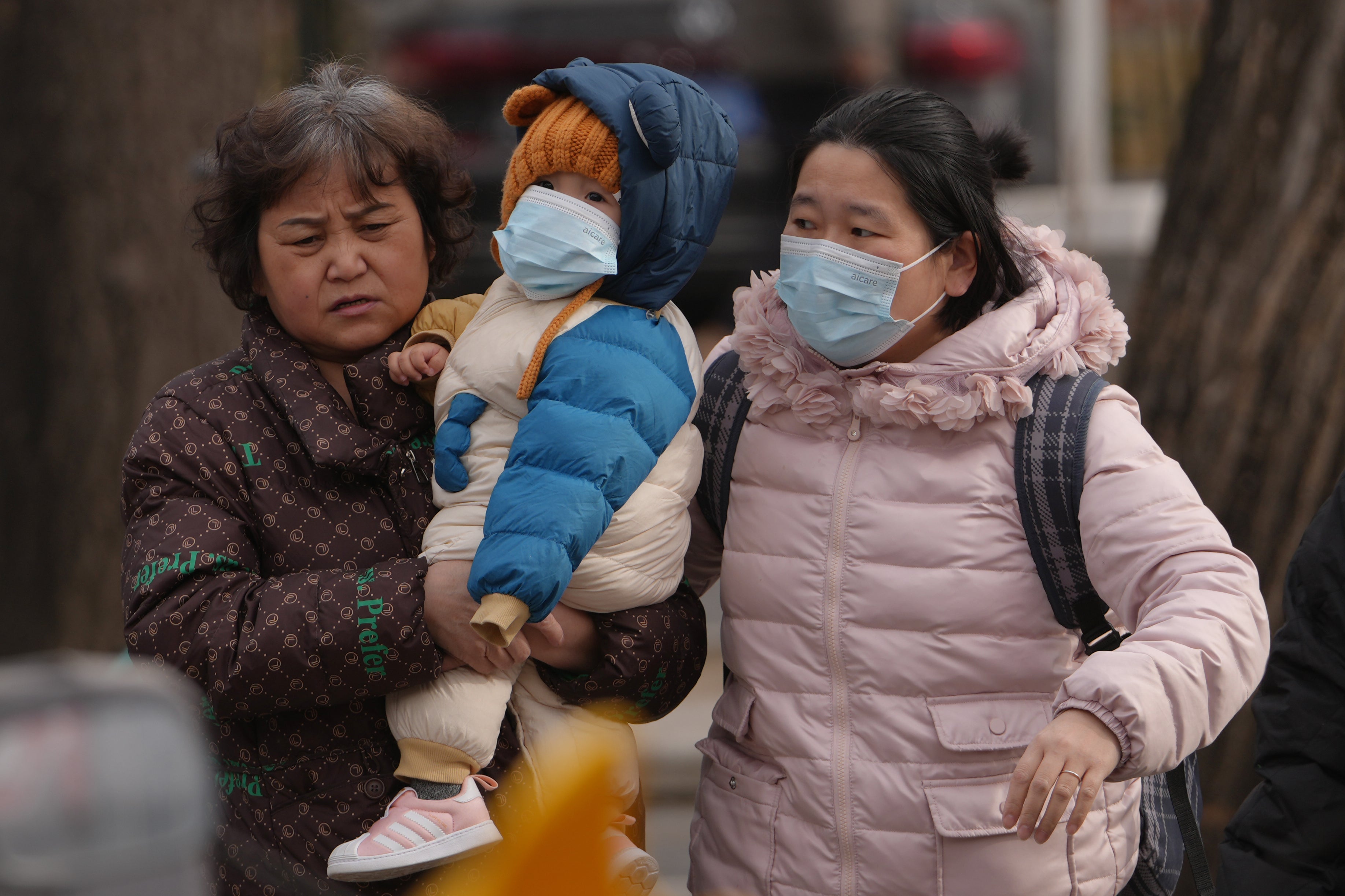 Women carry a toddler across a street in Beijing, Monday, Jan. 19, 2026. (AP Photo/Andy Wong)