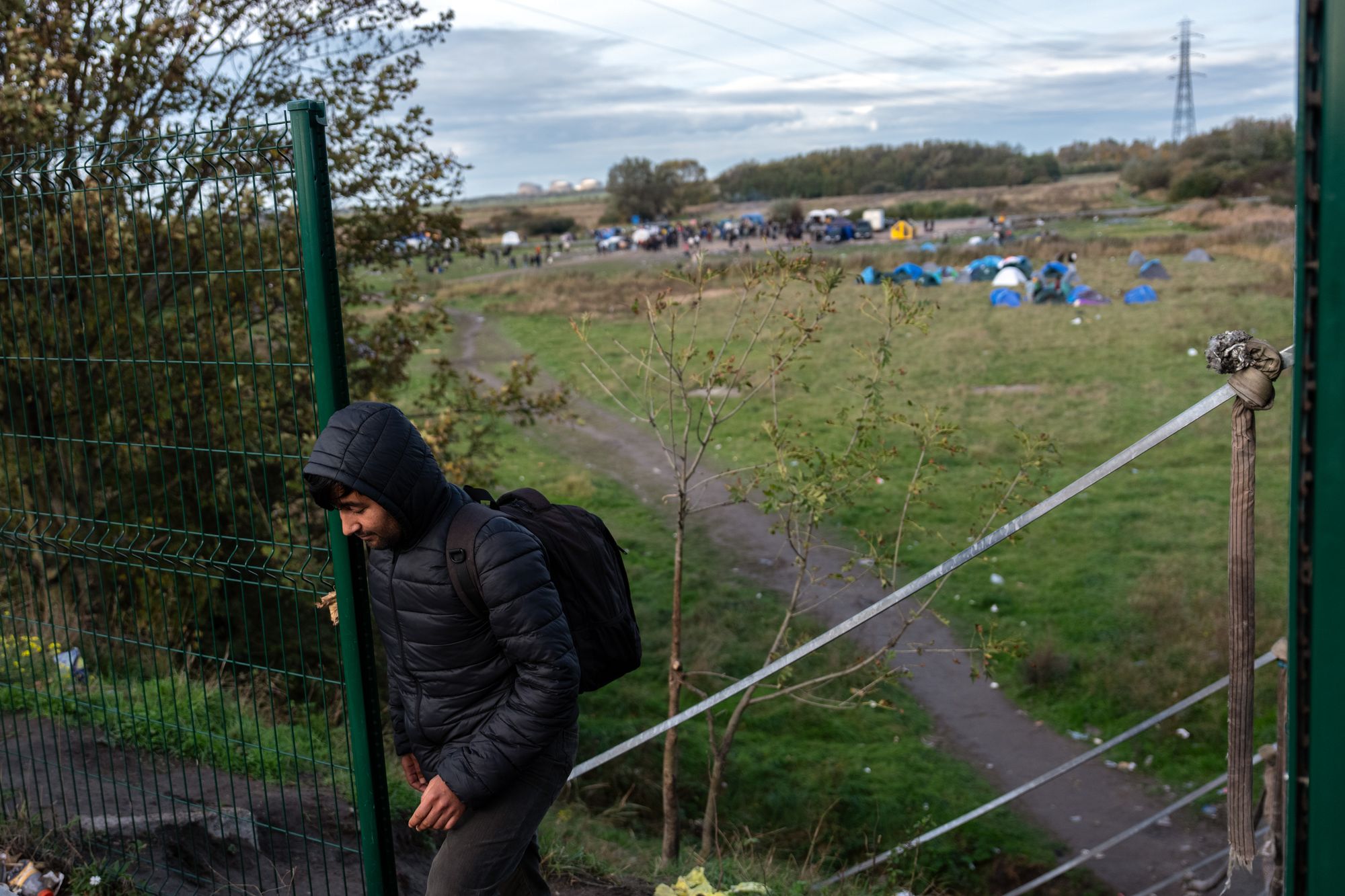 A man passes through a gap in a security fence near a migrant camp on October 31, 2025 in Loon-Plage, France.