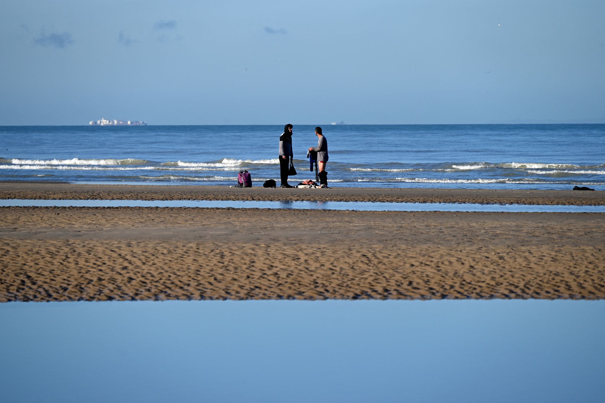 Migrants take off clothes after being rescued following their unsuccessful attempt to cross the Channel in a inflatable boat on a beach in Sangatte, northwestern France on December 13, 2025.