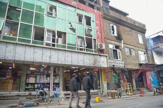 <p>People walk past the shattered glass of a building following an explosion in Kabul</p>