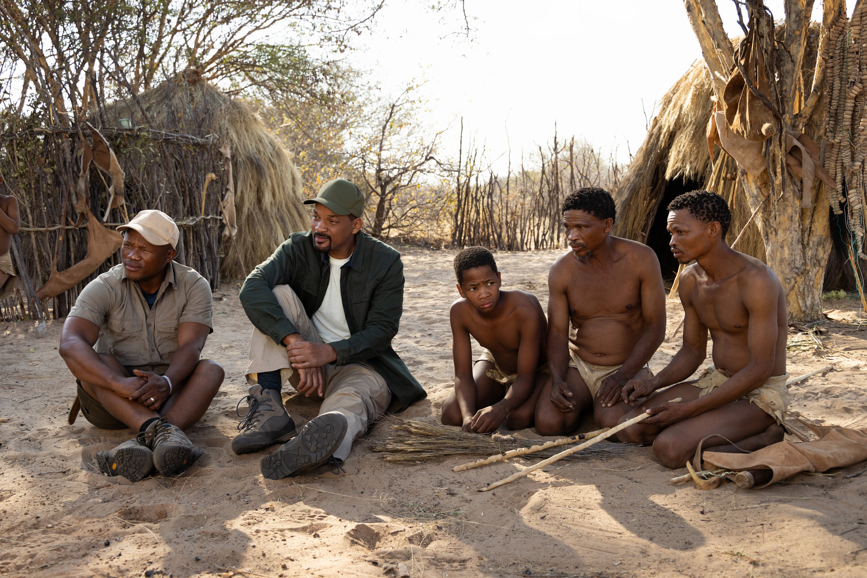 San bushman guide Kane Motswana, left, and Will Smith sit with the San people just before they learn how to start a fire in the Kalahari Desert