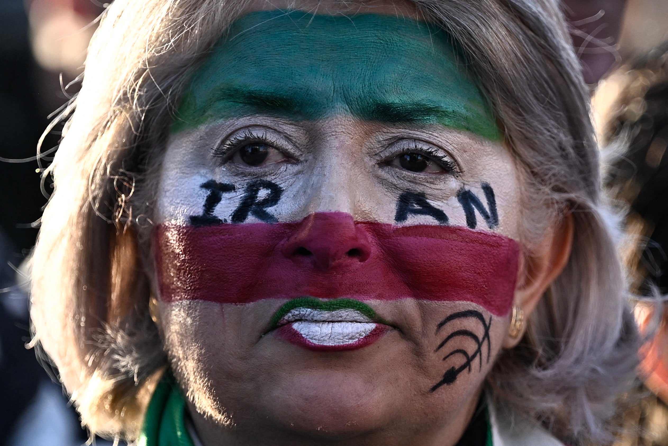 A protester wearing facepaint in Iranian national colours looks on during the March for Iran rally in support of the Iranian people, called by pro-royalists and supporters of the son of the last shah of Iran Mohammad Reza Pahlavi at the Place Victor Hugo, in Paris on January 18, 2026. (Photo by JULIEN DE ROSA / AFP via Getty Images)