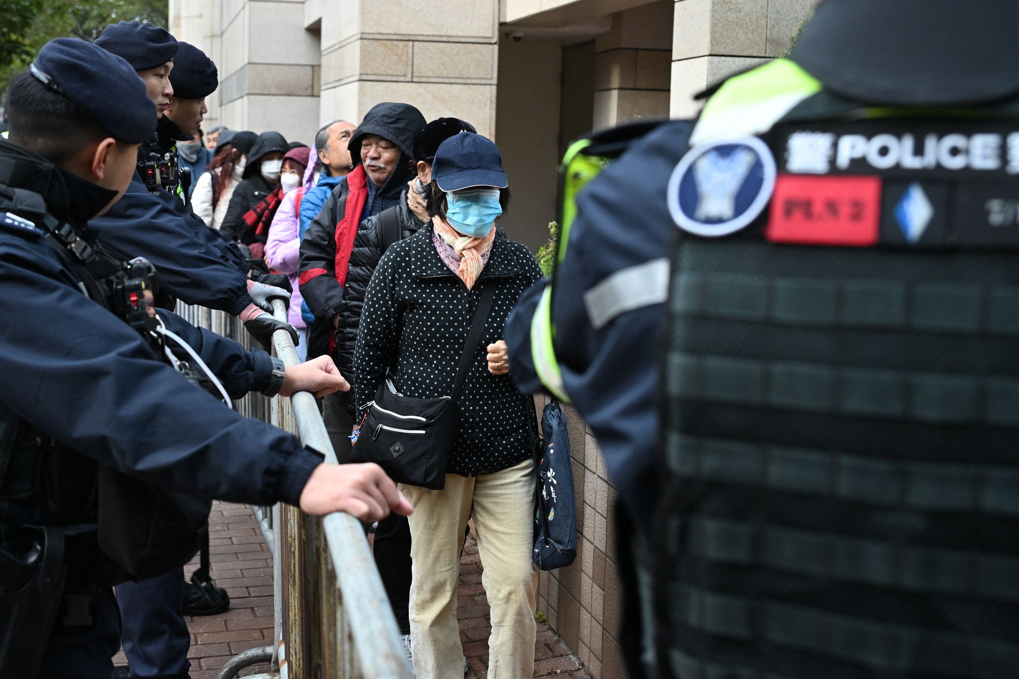 <p>Visitors pass by police as they enter  the West Kowloon Magistrates' court in Hong Kong on 22 January 2026, for the start of the trial of the now-disbanded Hong Kong Alliance with among the defendants three of its leaders, Chow Hang-tung, Albert Ho and LEE Cheuk-yan who for years organised the annual vigil for the victims of the Tiananmen Square massacre in 1989. (Photo by Peter PARKS / AFP via Getty Images)</p>