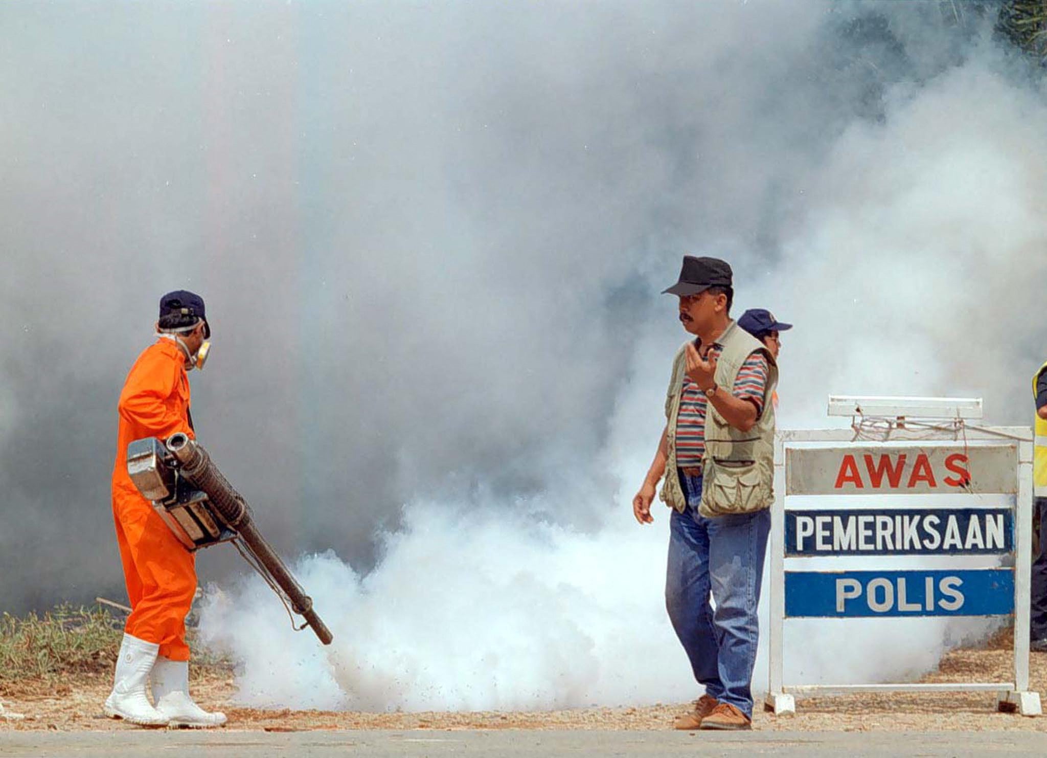 File. An official directs traffic while another fogs the area of Seelong in the southern state of Johor, 10 May 1999. - Malaysia extended its pig culling operation to Johor and the eastern state of Kelantan after tests showed positive results of the deadly Nipah virus in 40 pigs