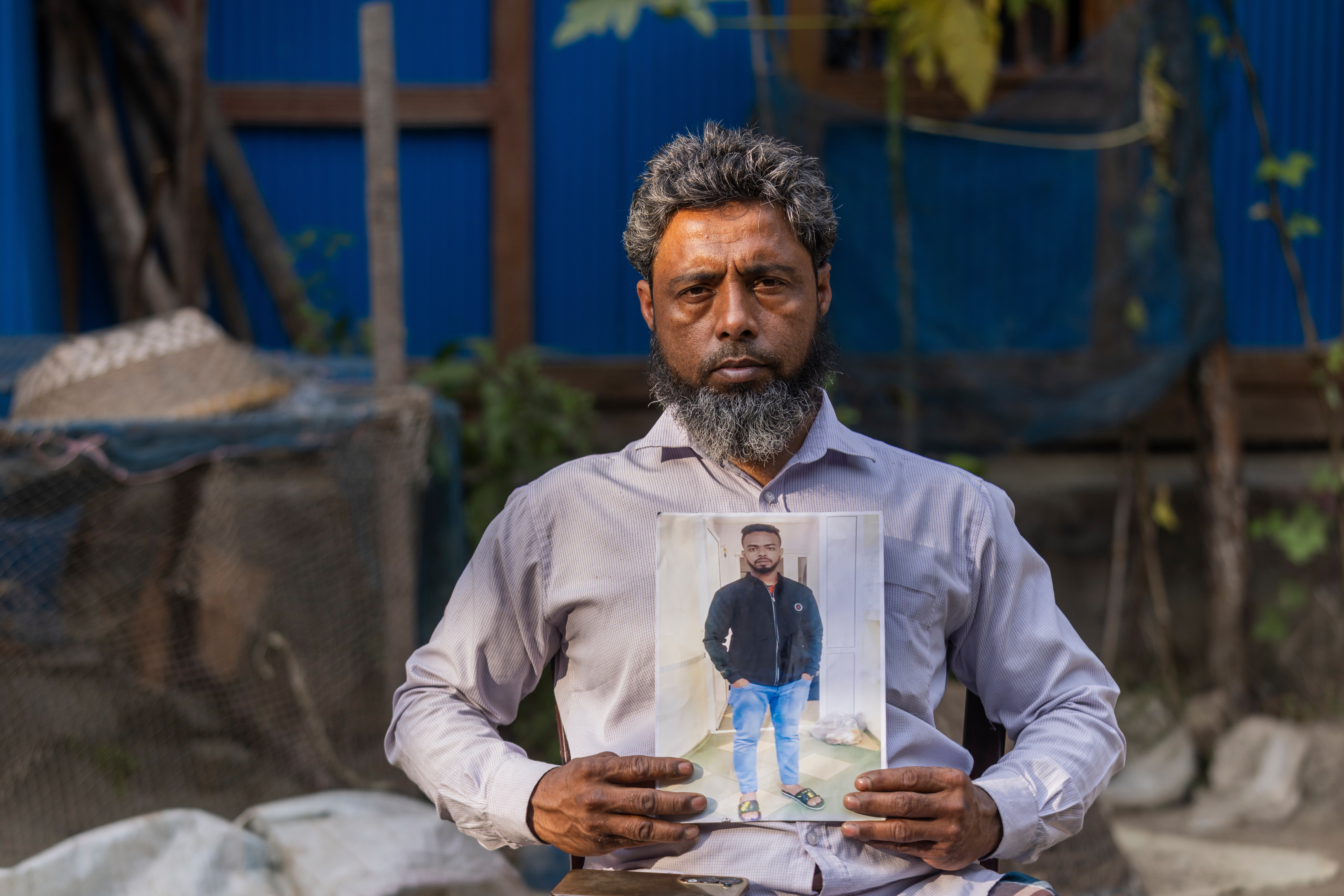 Mohammed Siraj holds a photograph of his 20-year-old son, Sajjad, who was killed after being taken to fight in Russia, at his home in Lakshmipur, Bangladesh, Dec. 10, 2025. (AP Photo/Rajib Dhar)