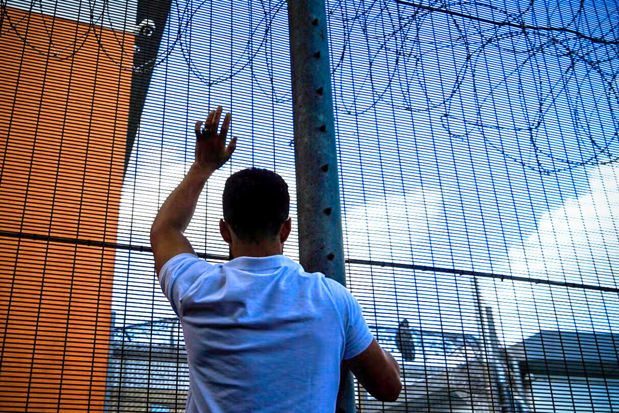 A protester communicates with those inside the perimeter fence of Brook House immigration removal centre, next to Gatwick airport