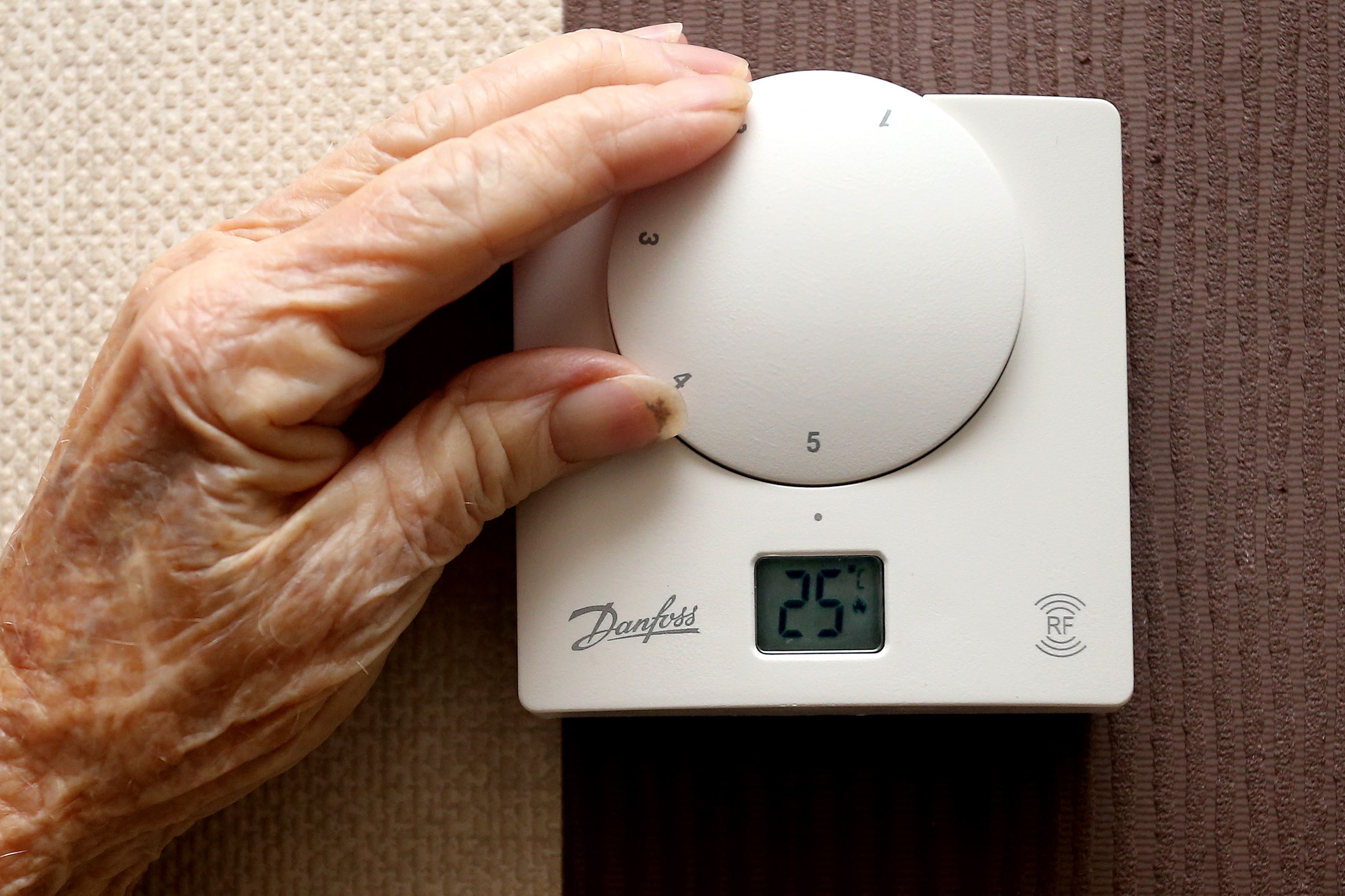 An elderly person adjusting a heating thermostat in a domestic home (PA)