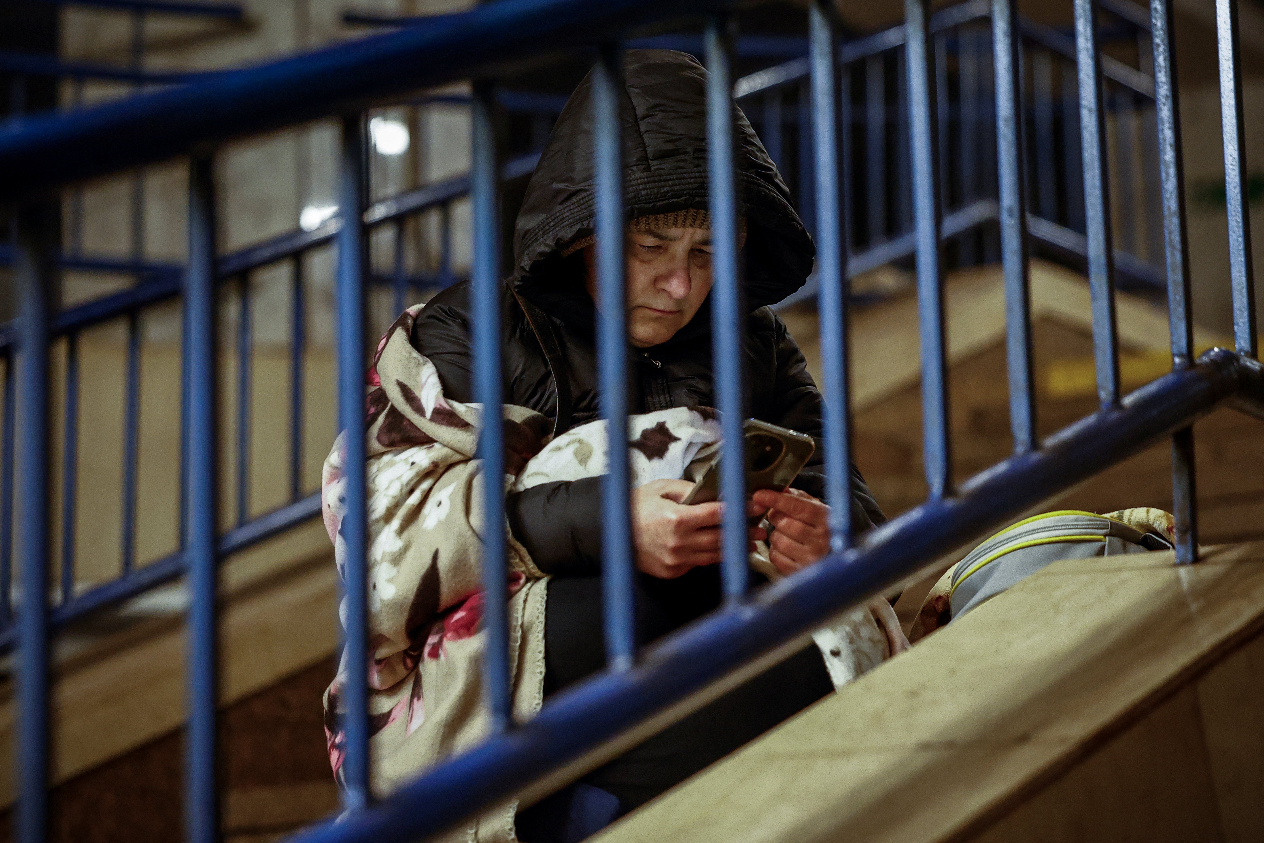 A woman checks her phone as she takes shelter inside a metro station during a Russian overnight missile and drone strike in Kyiv