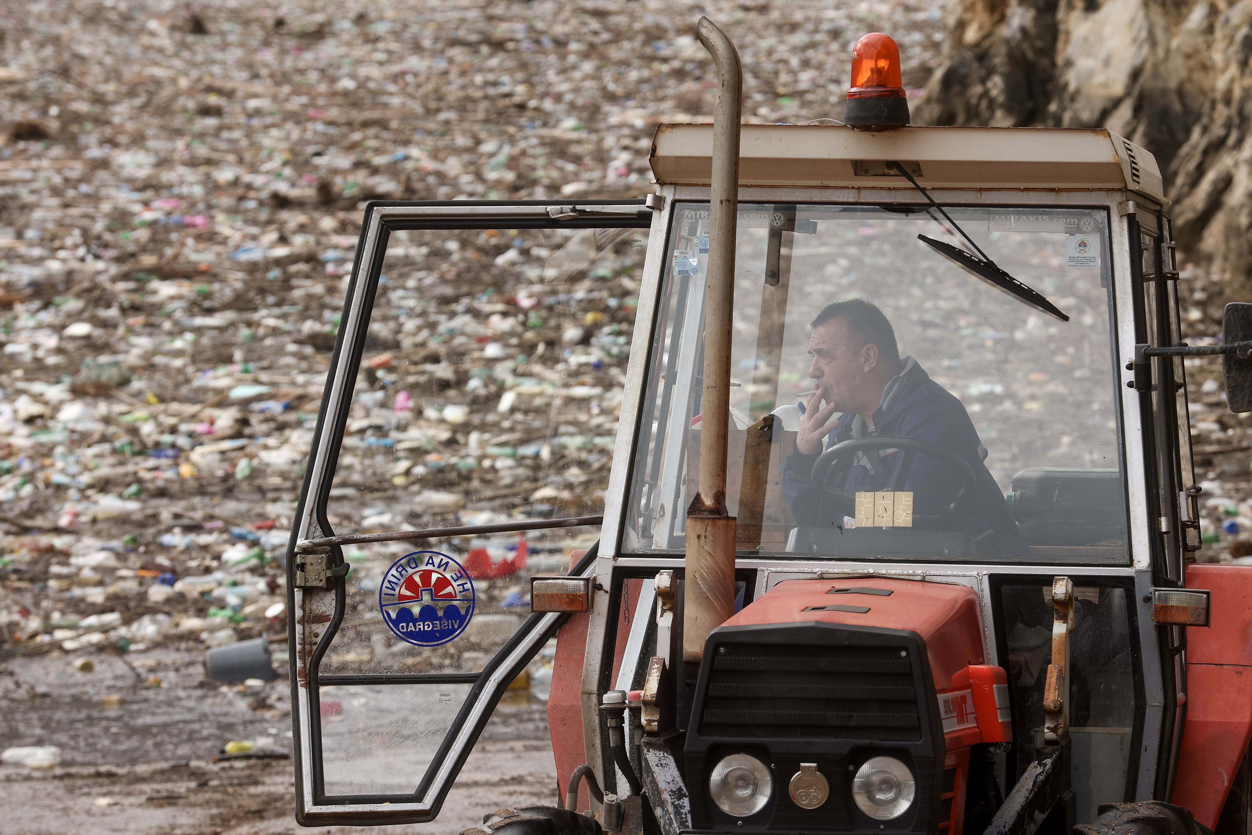 A worker takes a break, backdropped by tons of waste floating as it clogs the Drina river in Visegrad, Bosnia