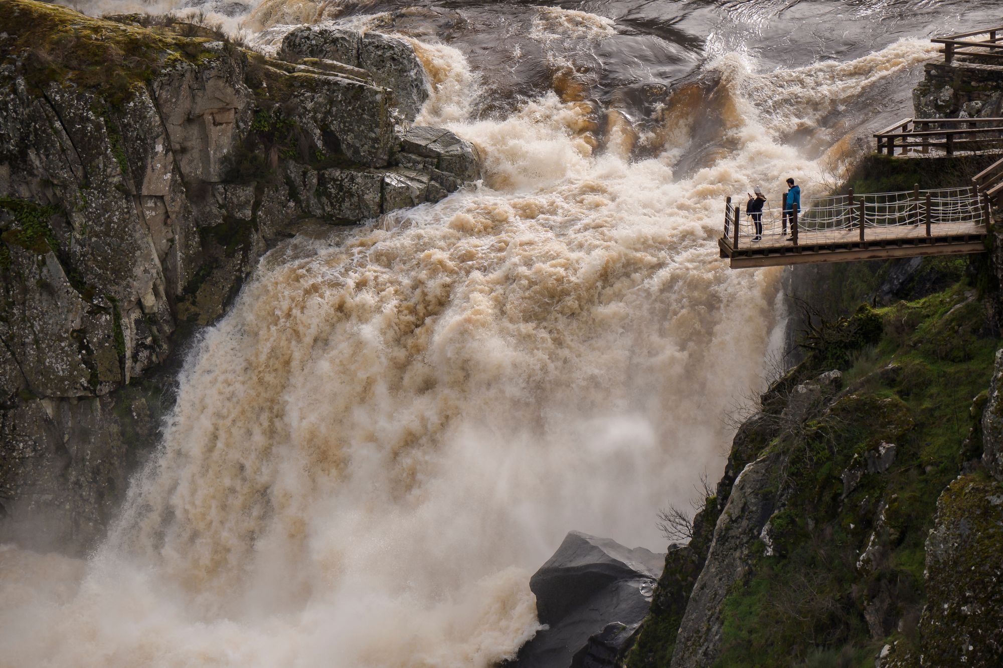 People watch as excess levels of water flow down the Pozo de los Humos waterfall