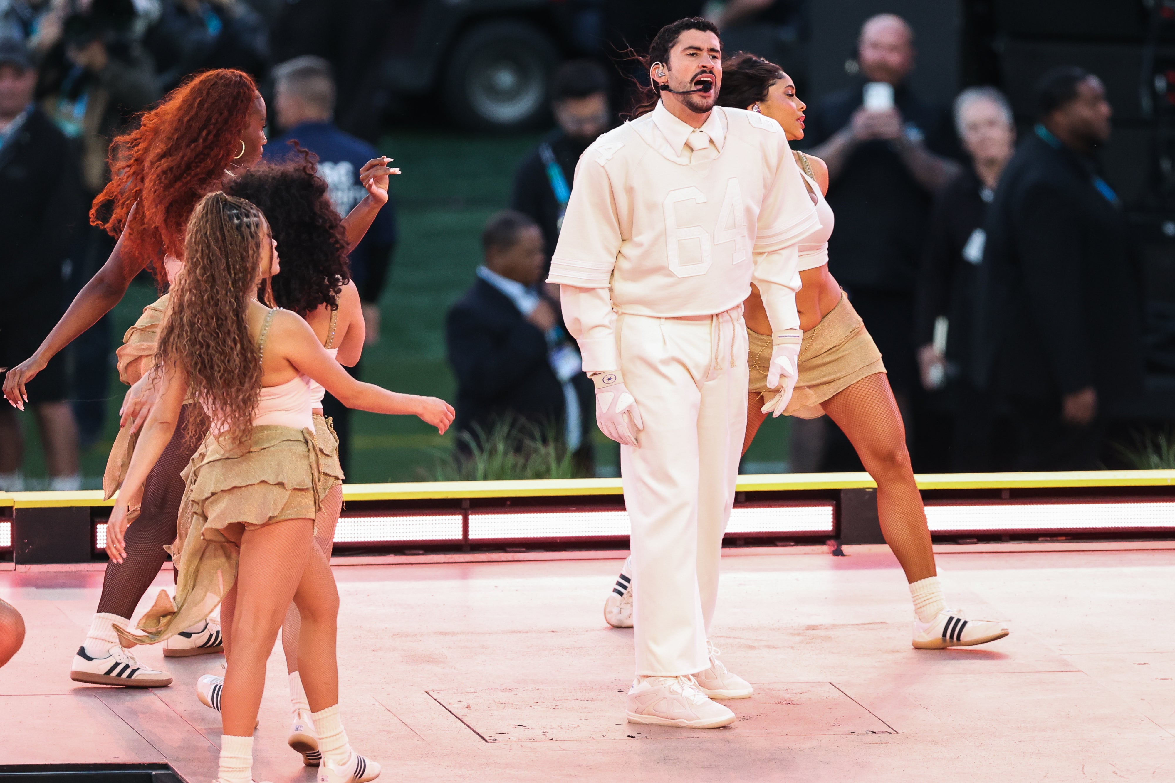 Bad Bunny wore an all-cream ensemble consisting of a collared shirt and tie, chinos and a sport-inspired jersey bearing the name “Ocasio” – his surname