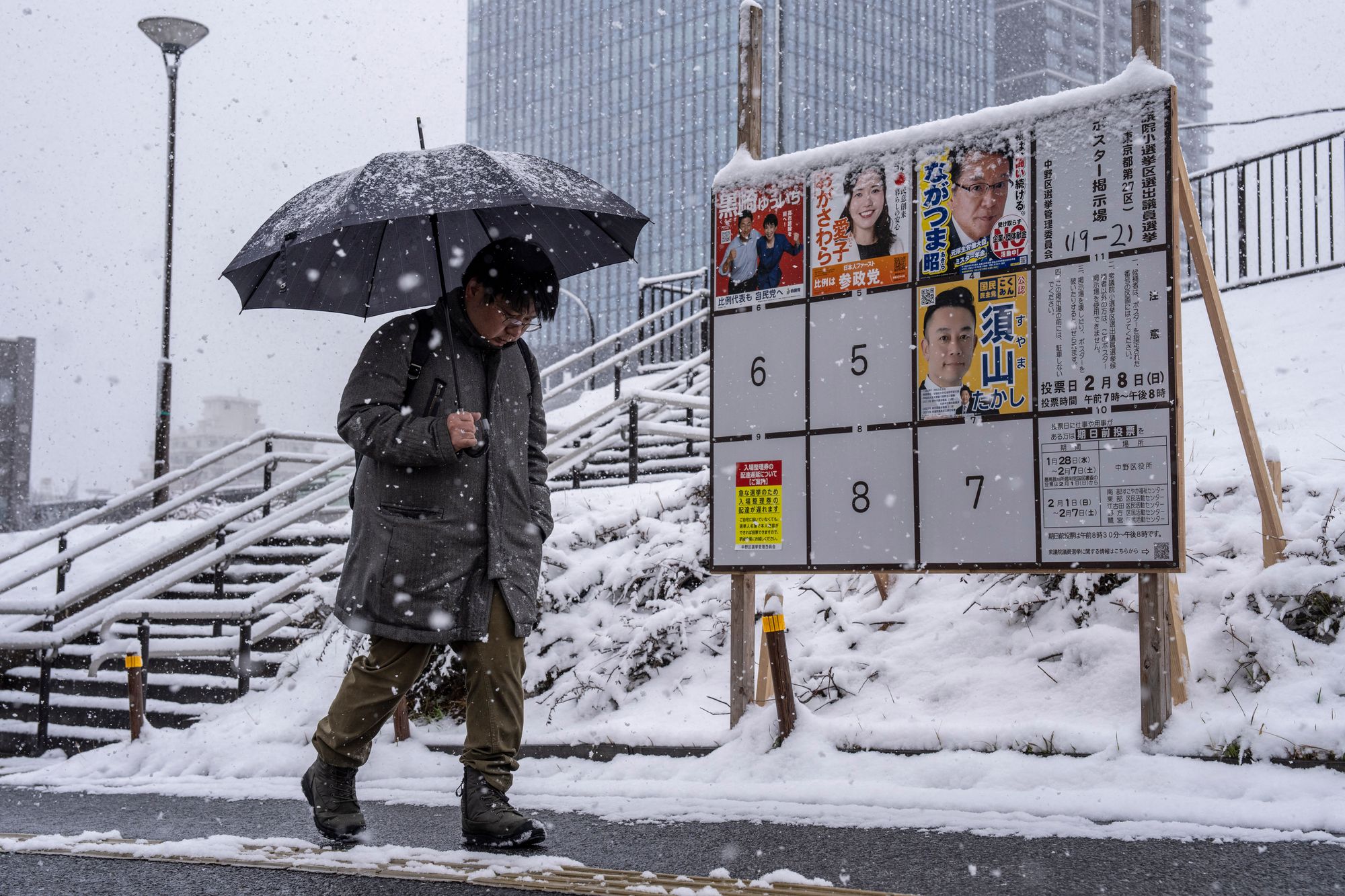 A man walks past a board displaying posters of candidates for the House of Representatives election during a snowfall in Tokyo on 8 February 2026