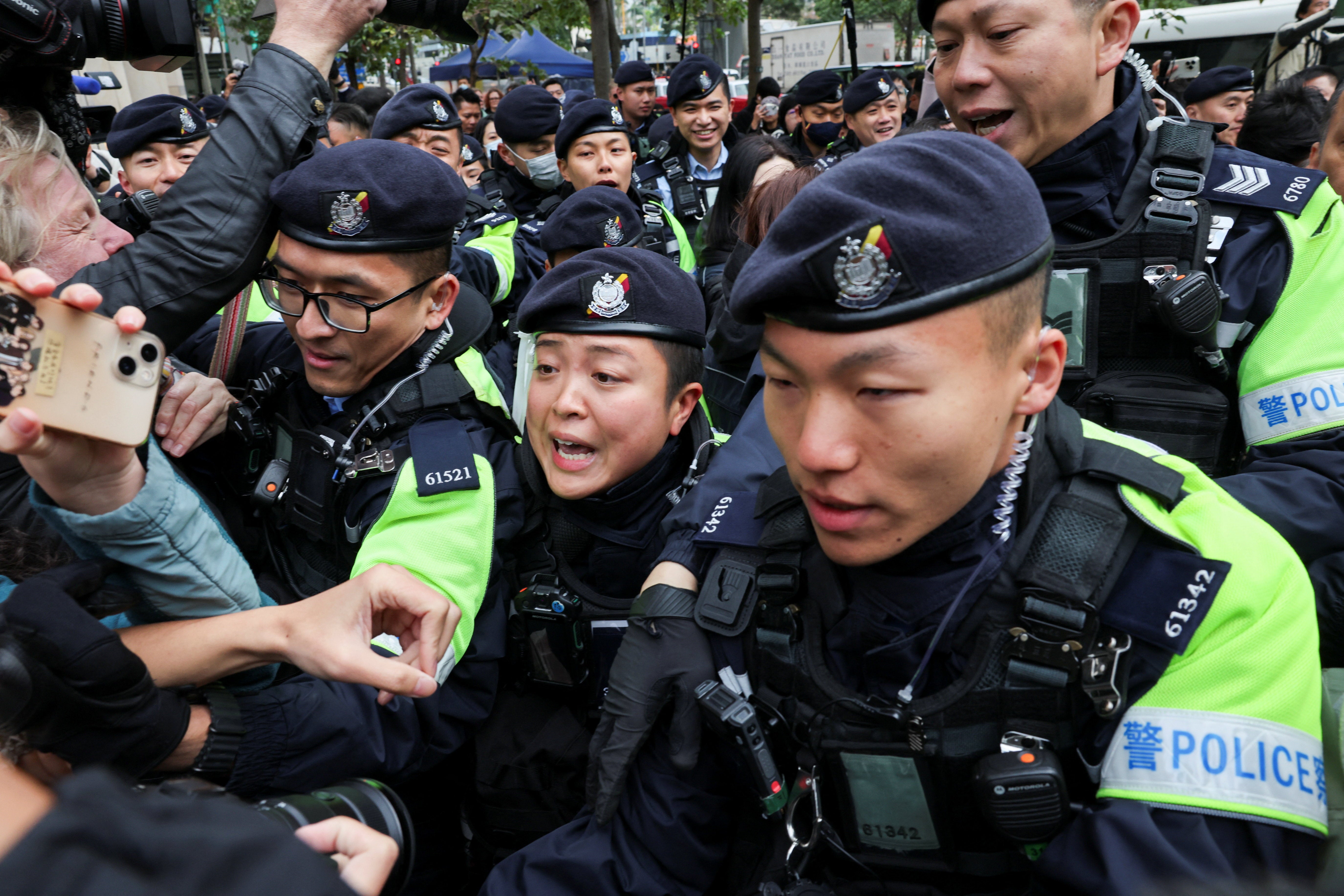 Police officers clear the way for retired bishop Cardinal Joseph Zen Ze-kiun and Teresa Lai, wife of Jimmy Lai, as they leave West Kowloon Magistrates' Courts building after Jimmy Lai, founder of the now-defunct pro-democracy newspaper Apple Daily, was sentenced a total of 20 years in jail