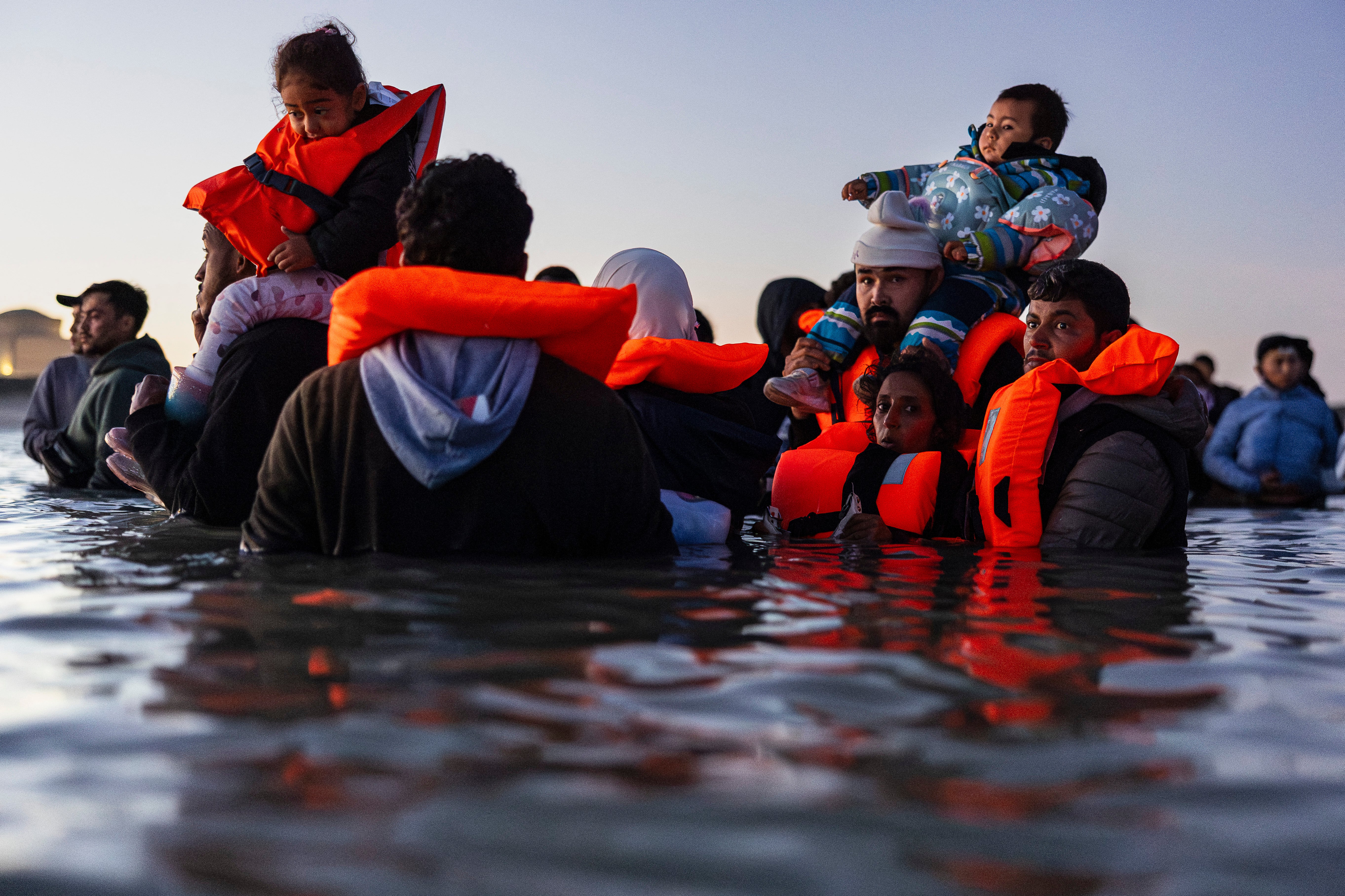 Migrants carrying children wait in the water to try to board a smuggler's boat in an attempt to cross the English Channel off the beach of Gravelines, northern France on September 19, 2025.