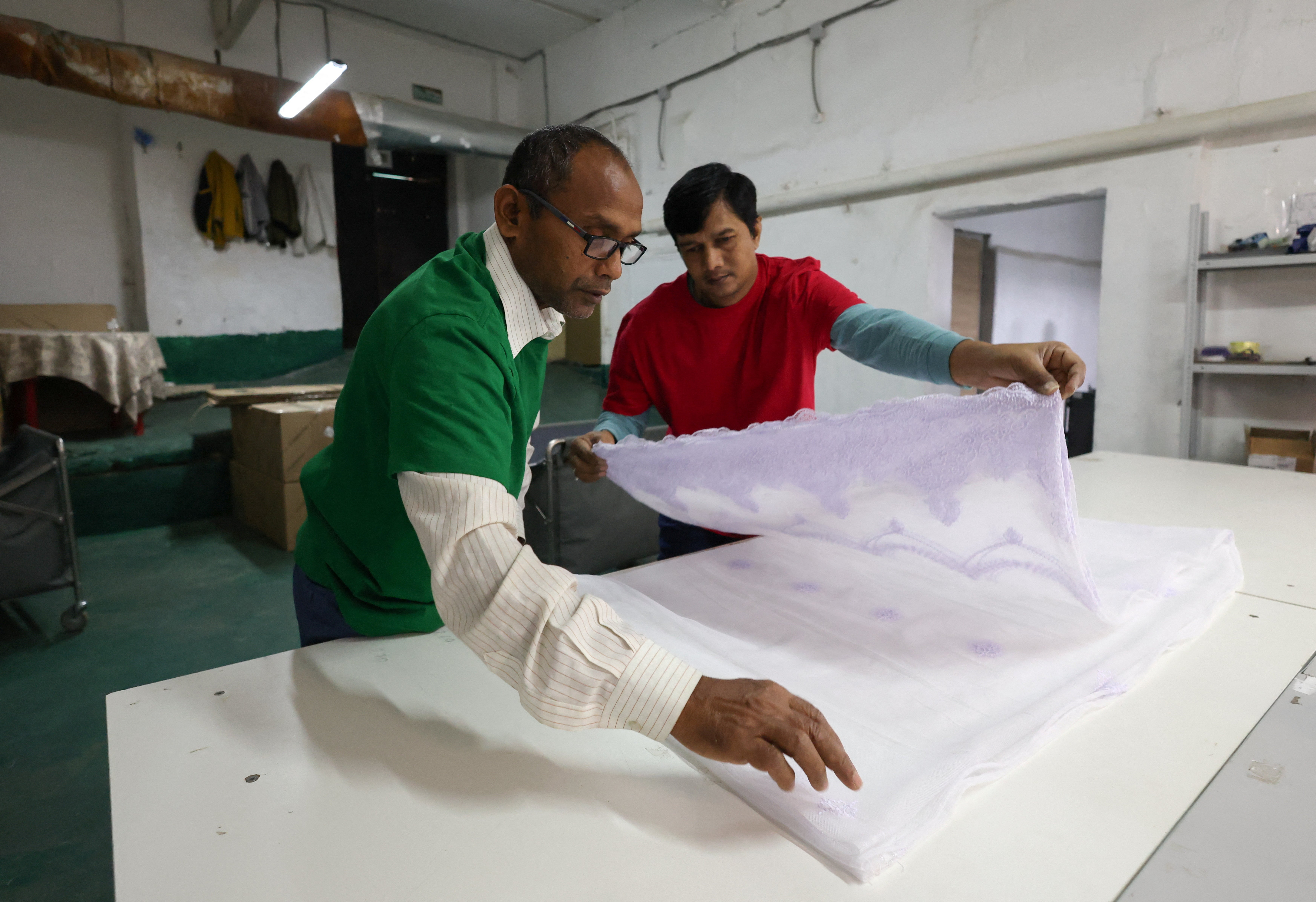 Kumar, 50, and Bharat, 40 (no last names given), migrant workers from India, fold tulle fabric at a textile factory in the town of Balashikha outside Moscow, Russia