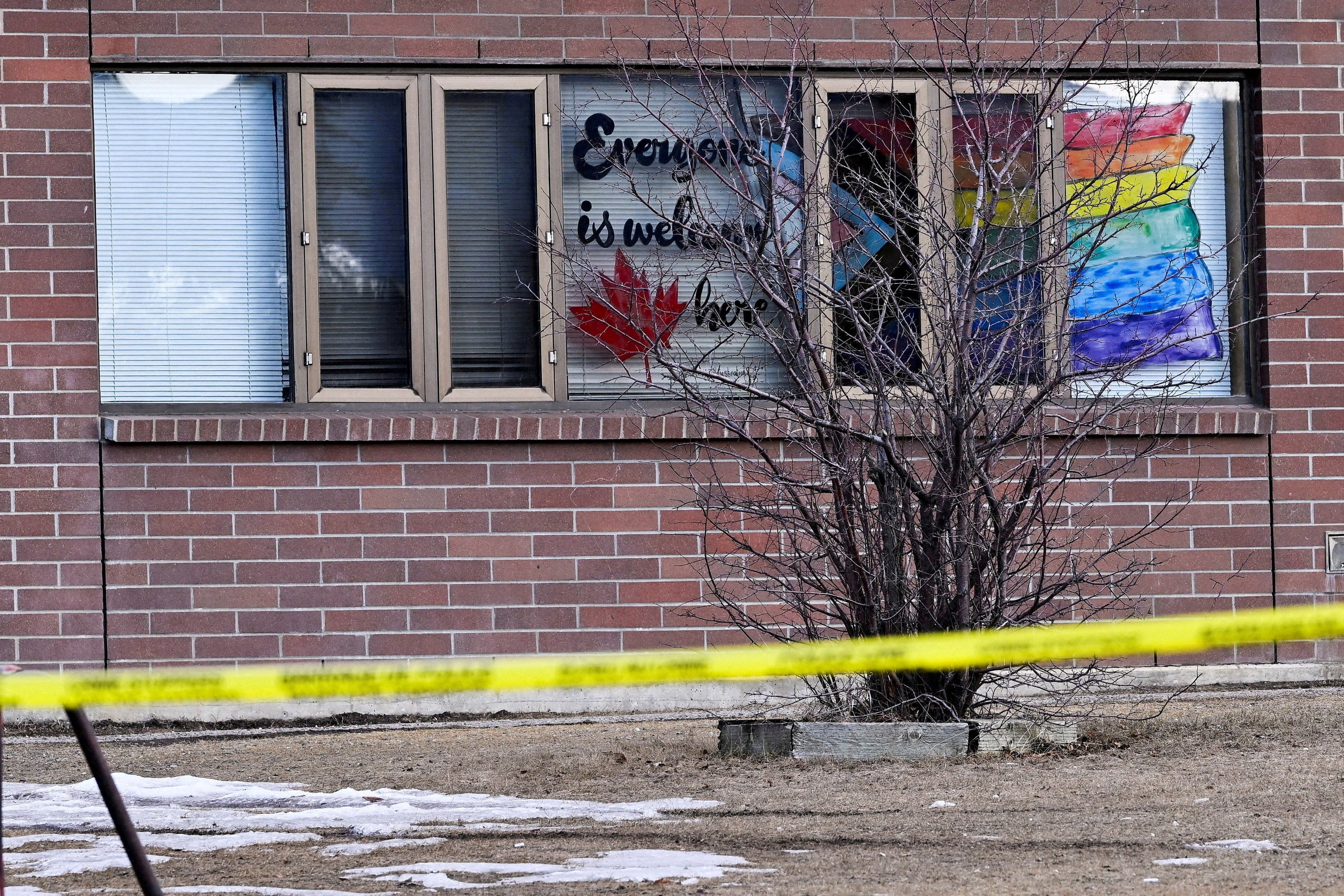 Police tape surrounds the high school with an 'Everyone is welcome here' message painted on a window