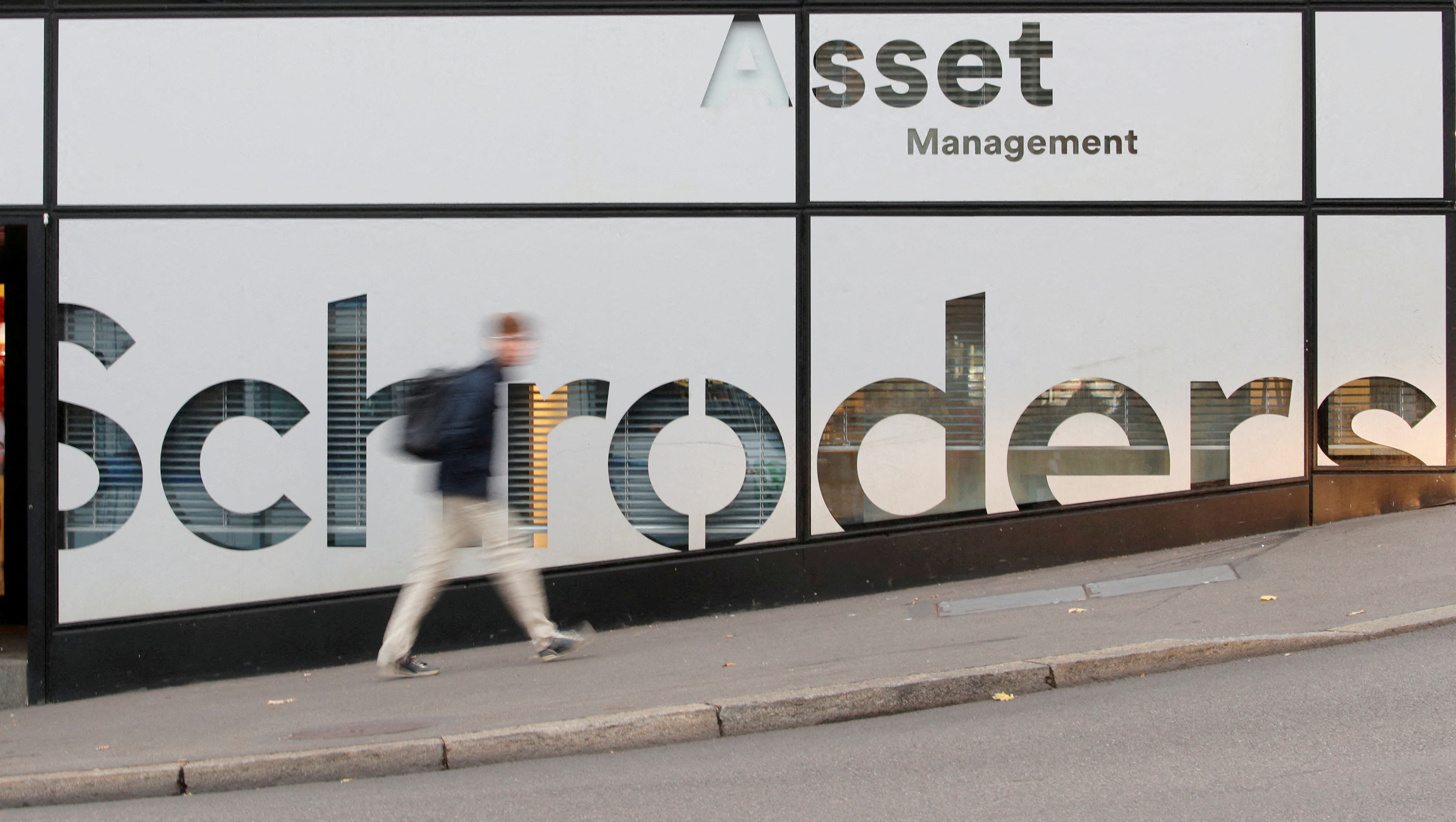 A man walks past the logo of investment management company Schroders at a branch in Zurich, Switzerland.