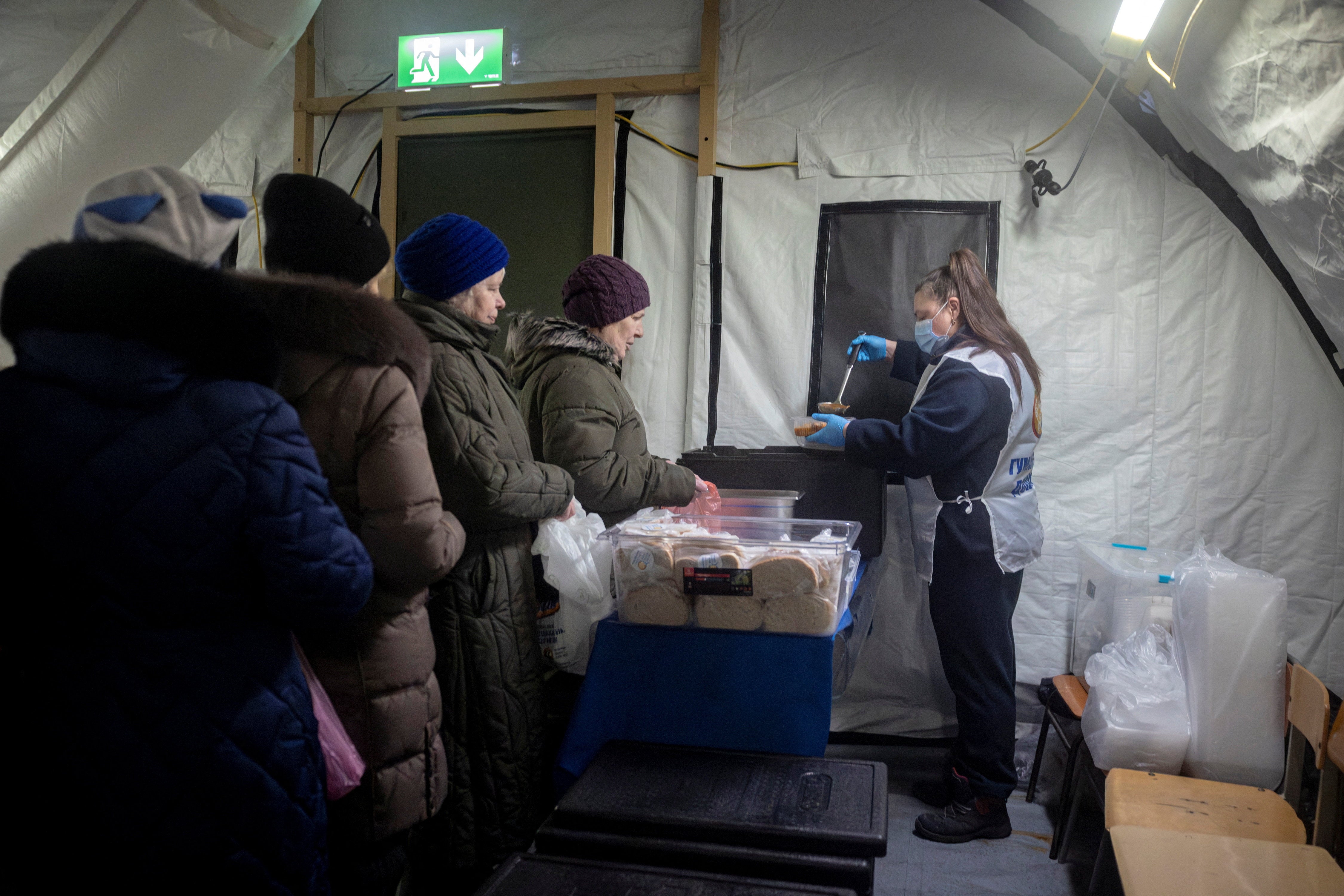 People receive a free warm meal from Central World Kitchen in a heated tent of the emergency services in a neighbourhood where many apartments are left without electricity