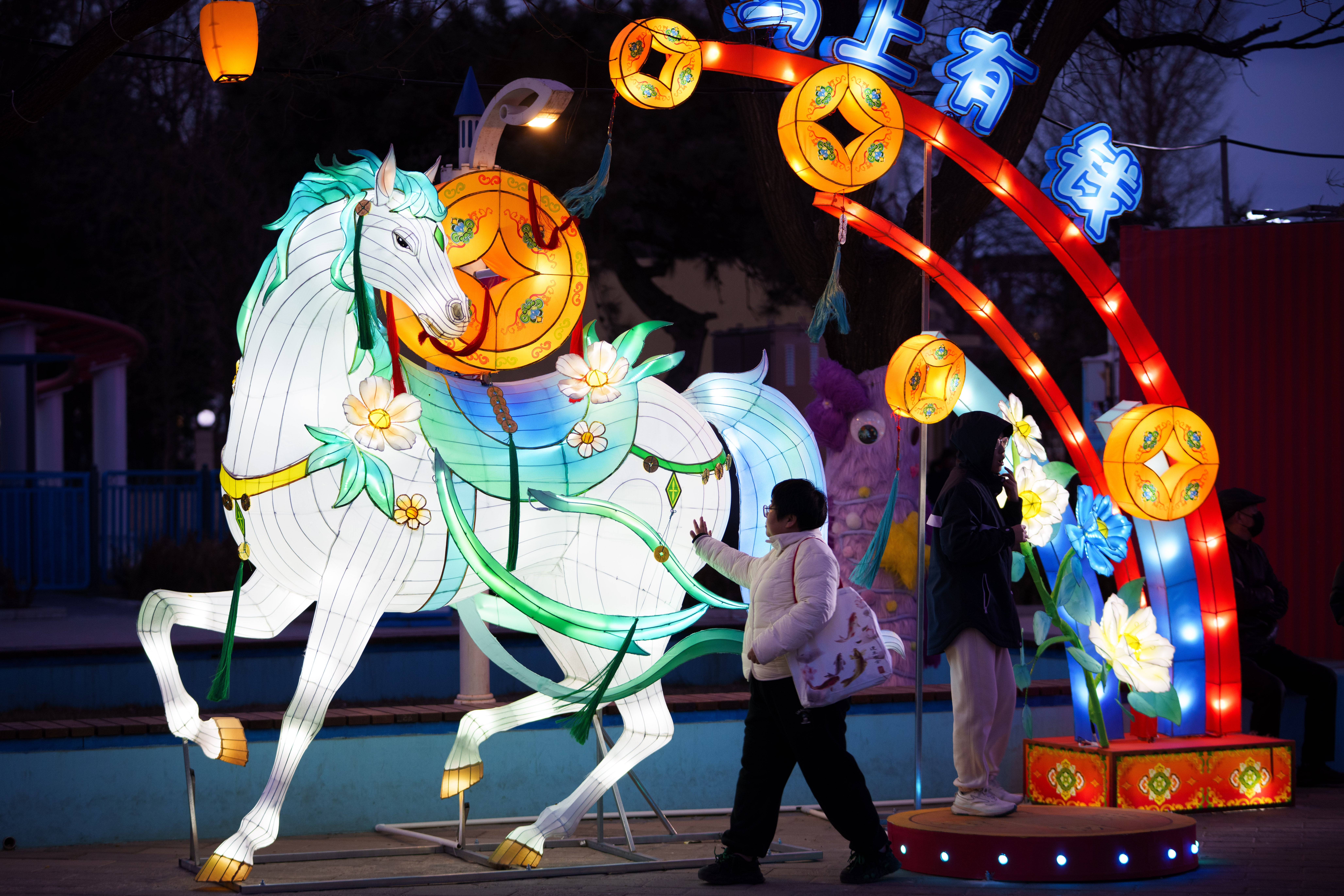 Visitors walk past an illuminated horse lantern display ahead of Lunar New Year celebrations at an amusement park on the outskirts of Beijing, China.