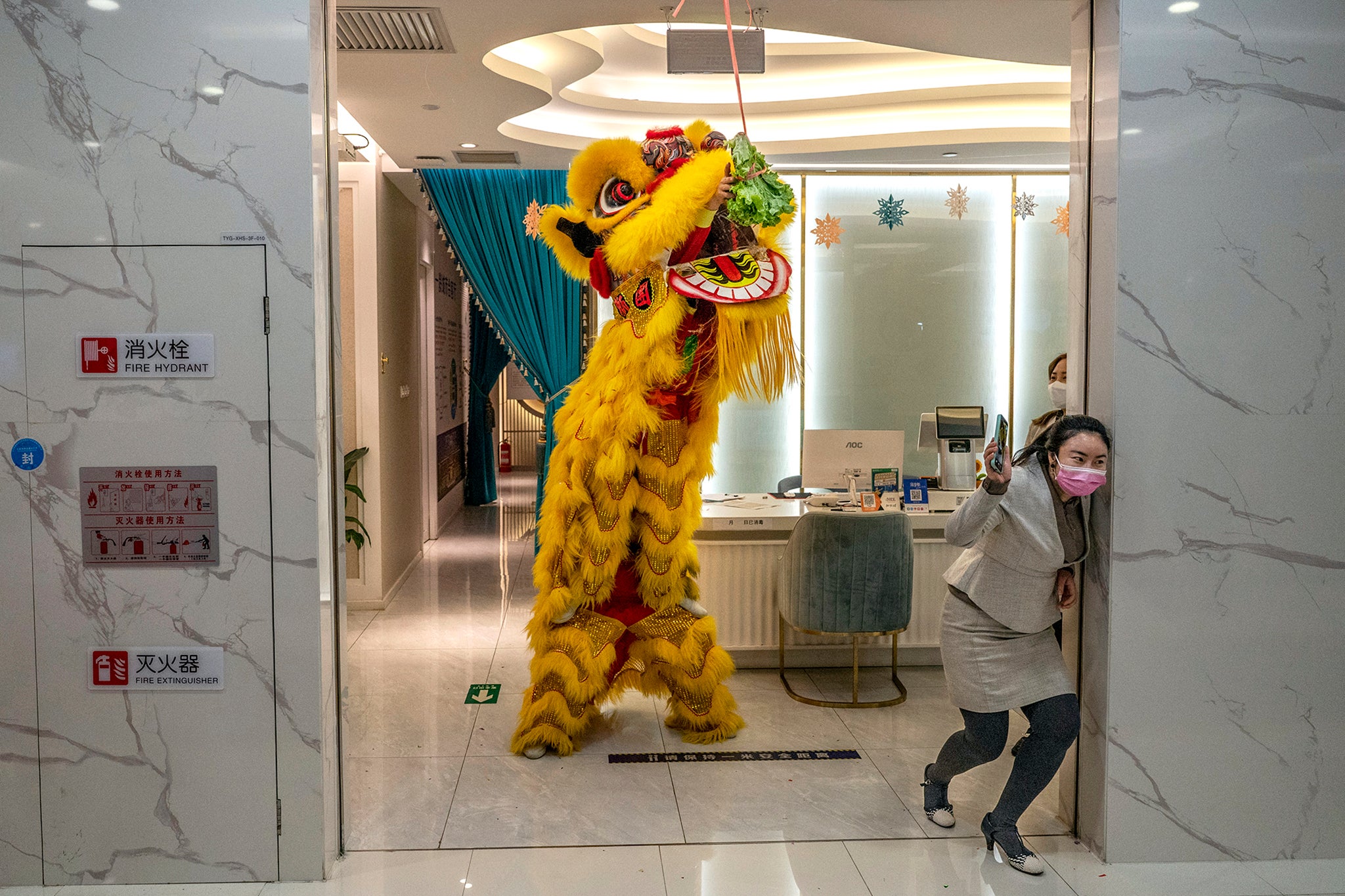 Продавач истрчава на врата док традиционални лавовски плесач посеже да узме понуду зелене салате која виси са врата у тржном центру у Пекингу