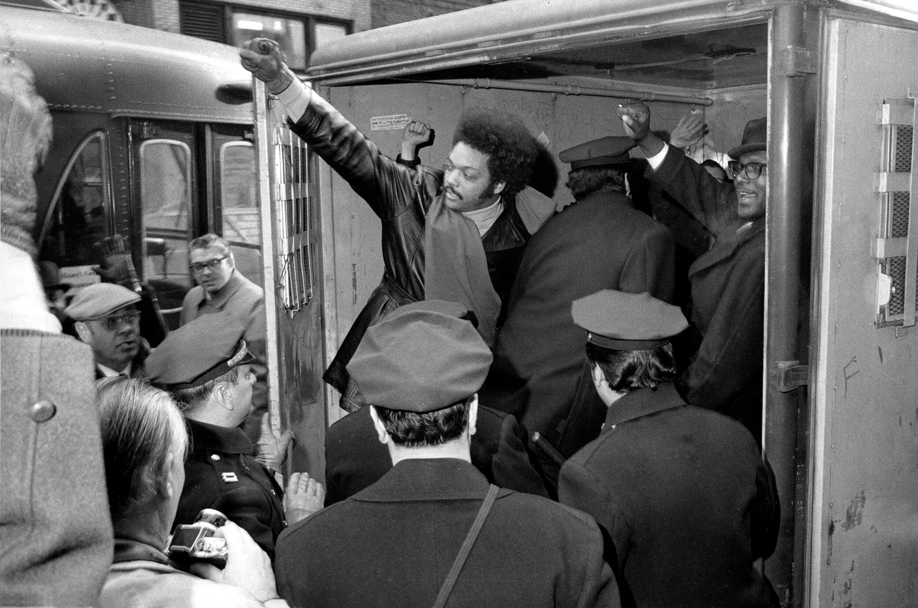 Jesse Jackson raises a clenched fist from a police van after he and 11 others from Operation Breadbasket were arrested during a New York sit-in in 1971