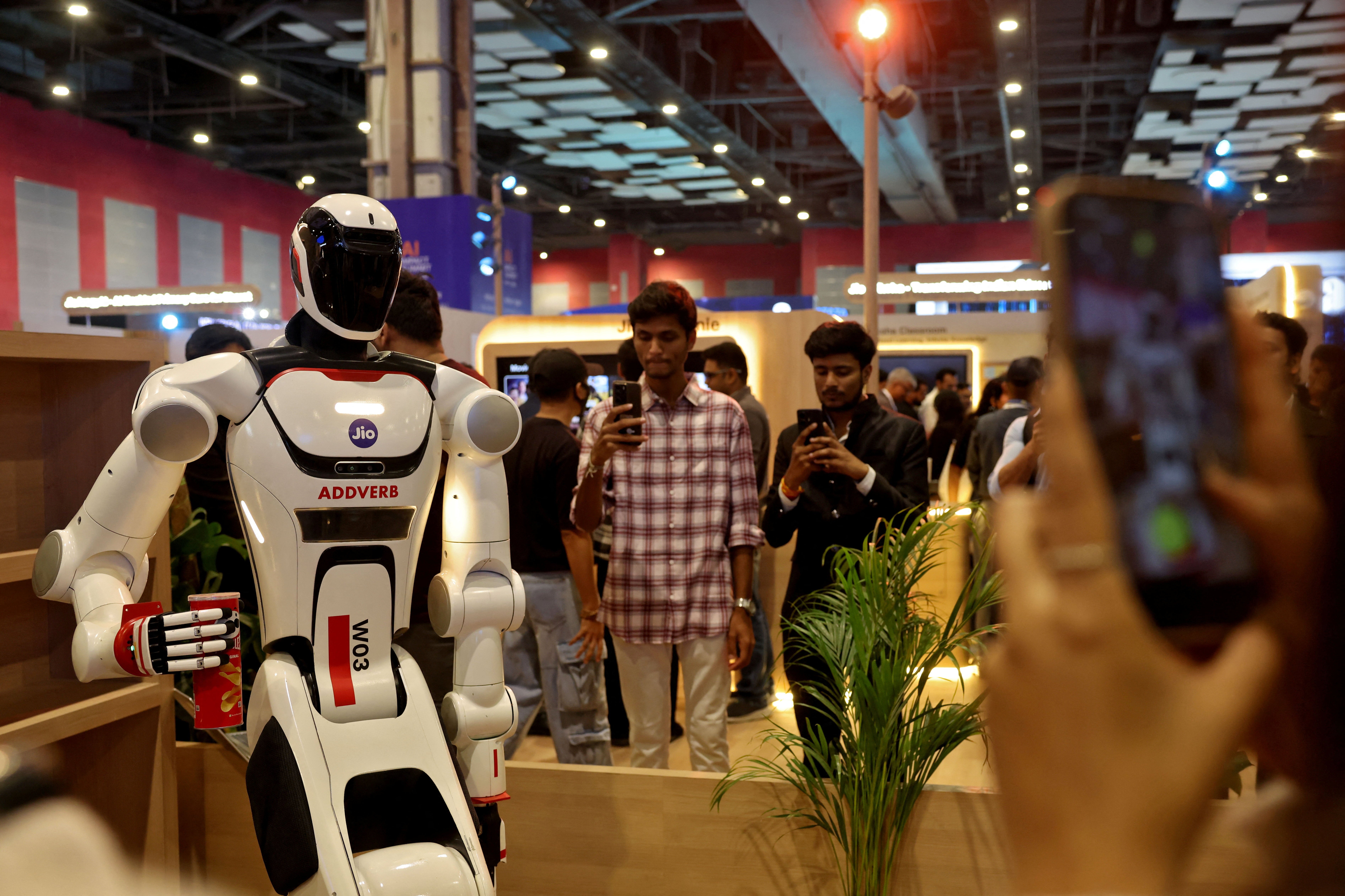 Visitors use their mobile phones to take pictures of a Jio humanoid robot named Elixis at Bharat Mandapam, one of the venues for AI Impact Summit