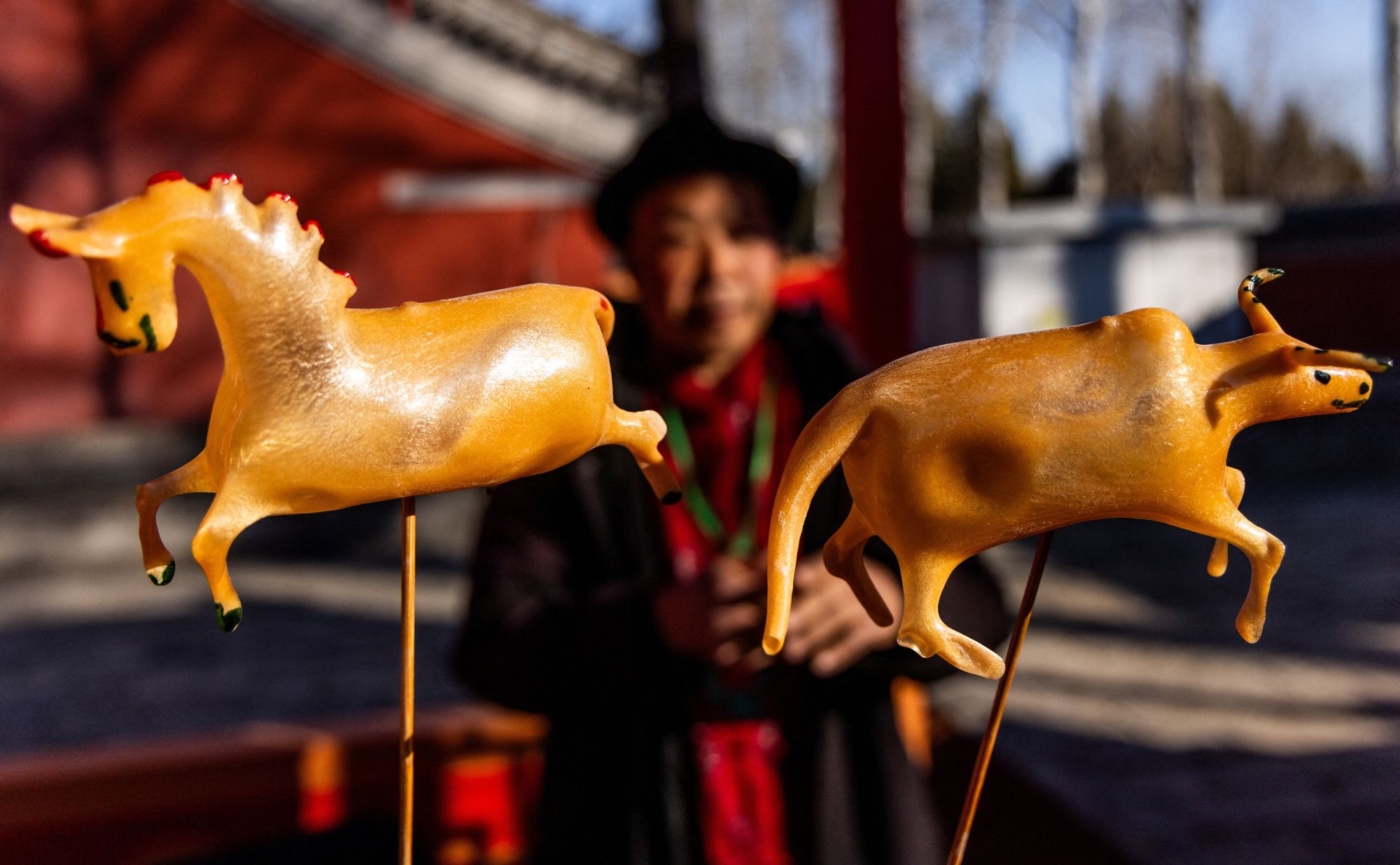 A vendor looks on through figures of a horse and an ox at a holiday street market on the first day of the Lunar New Year of the Horse at the Niangniang Temple in Beijing, China.