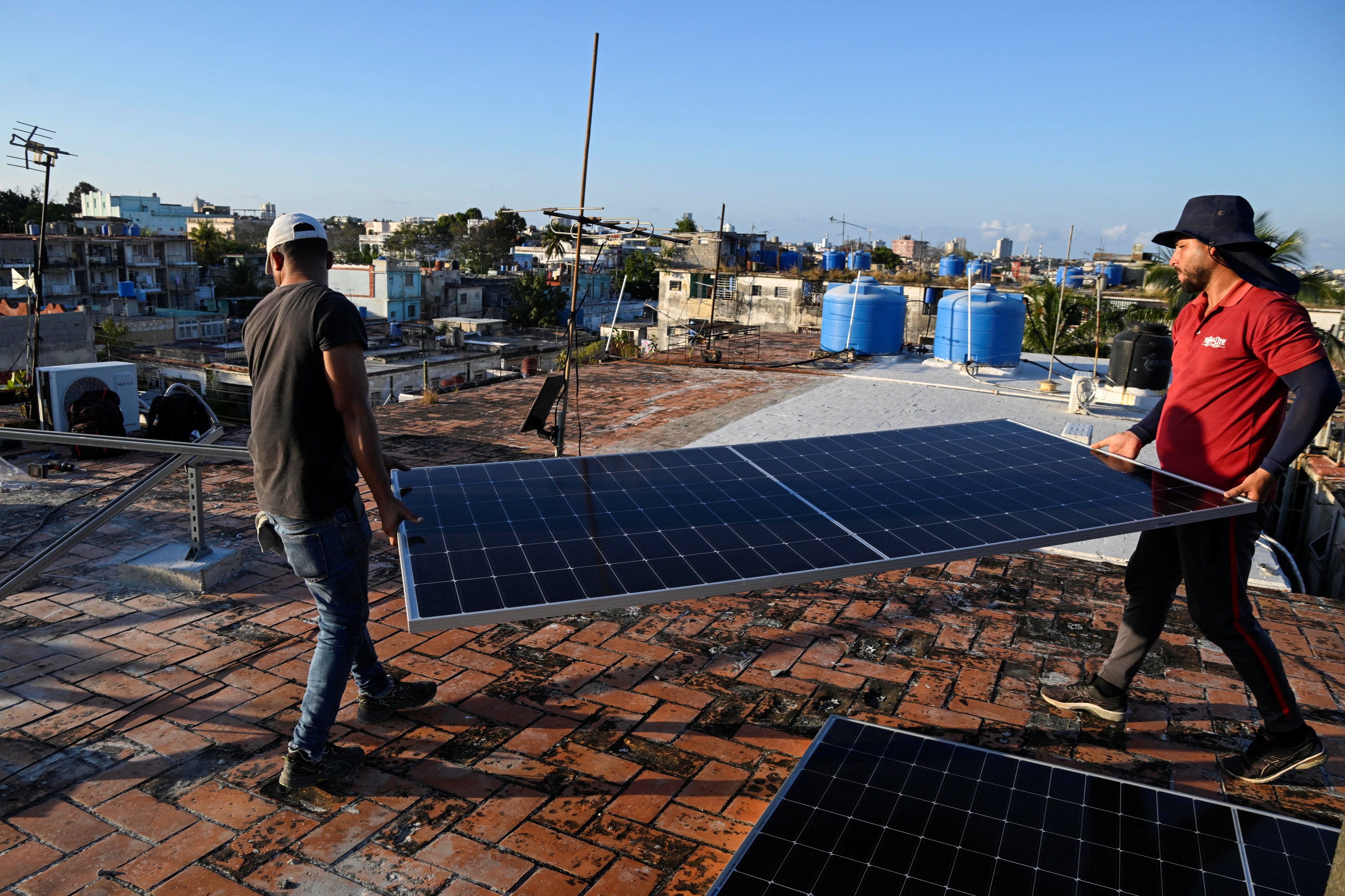 Solar panel technicians Denis Tamayo, 30, and Alejandro Guerra, 30, carry a solar panel on the rooftop of a building as Cubans grapple with an ongoing energy crisis exacerbated by fuel shortages