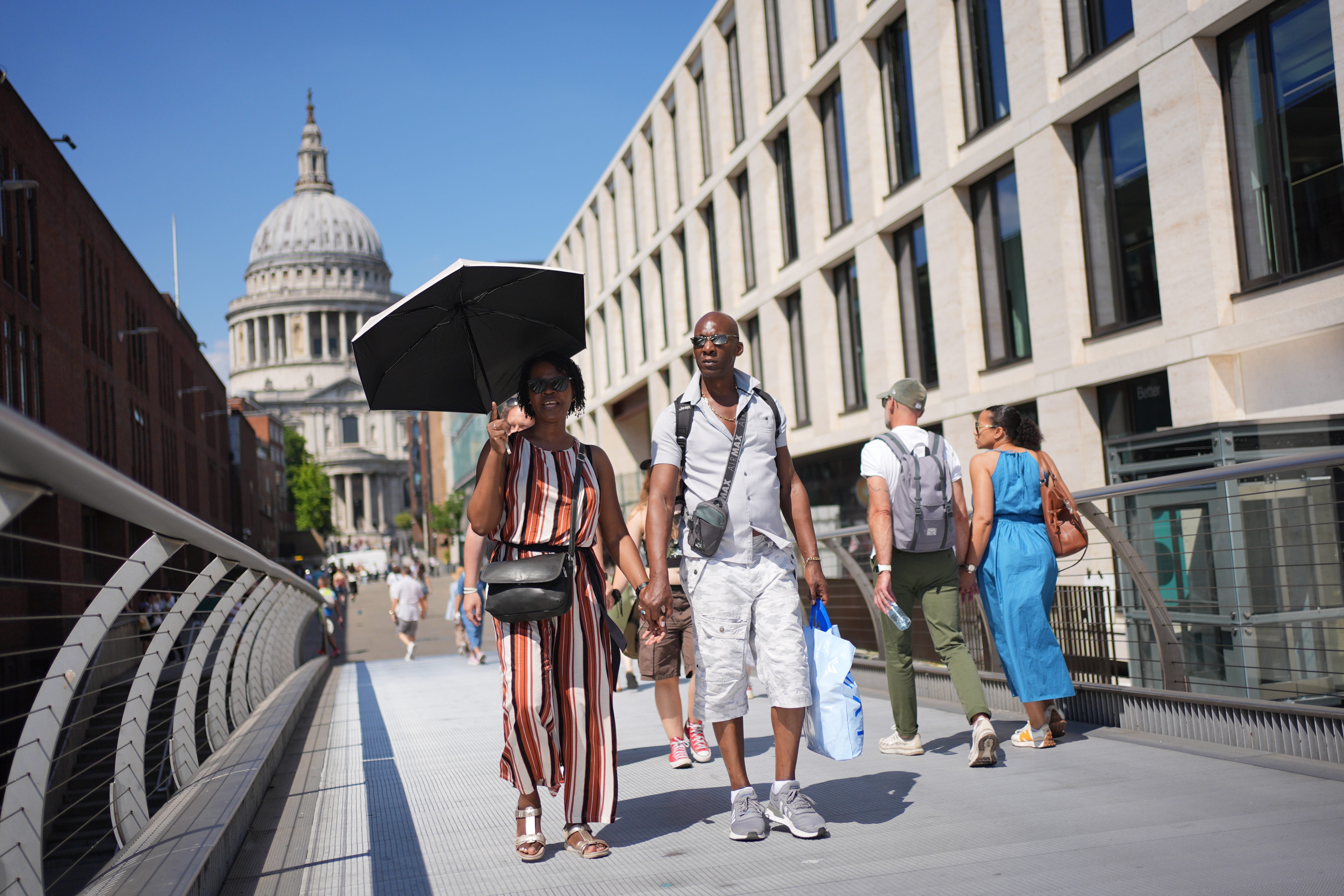 People shield from the sun under an umbrella, on the Millennium Bridge in London (Yui Mok/PA)